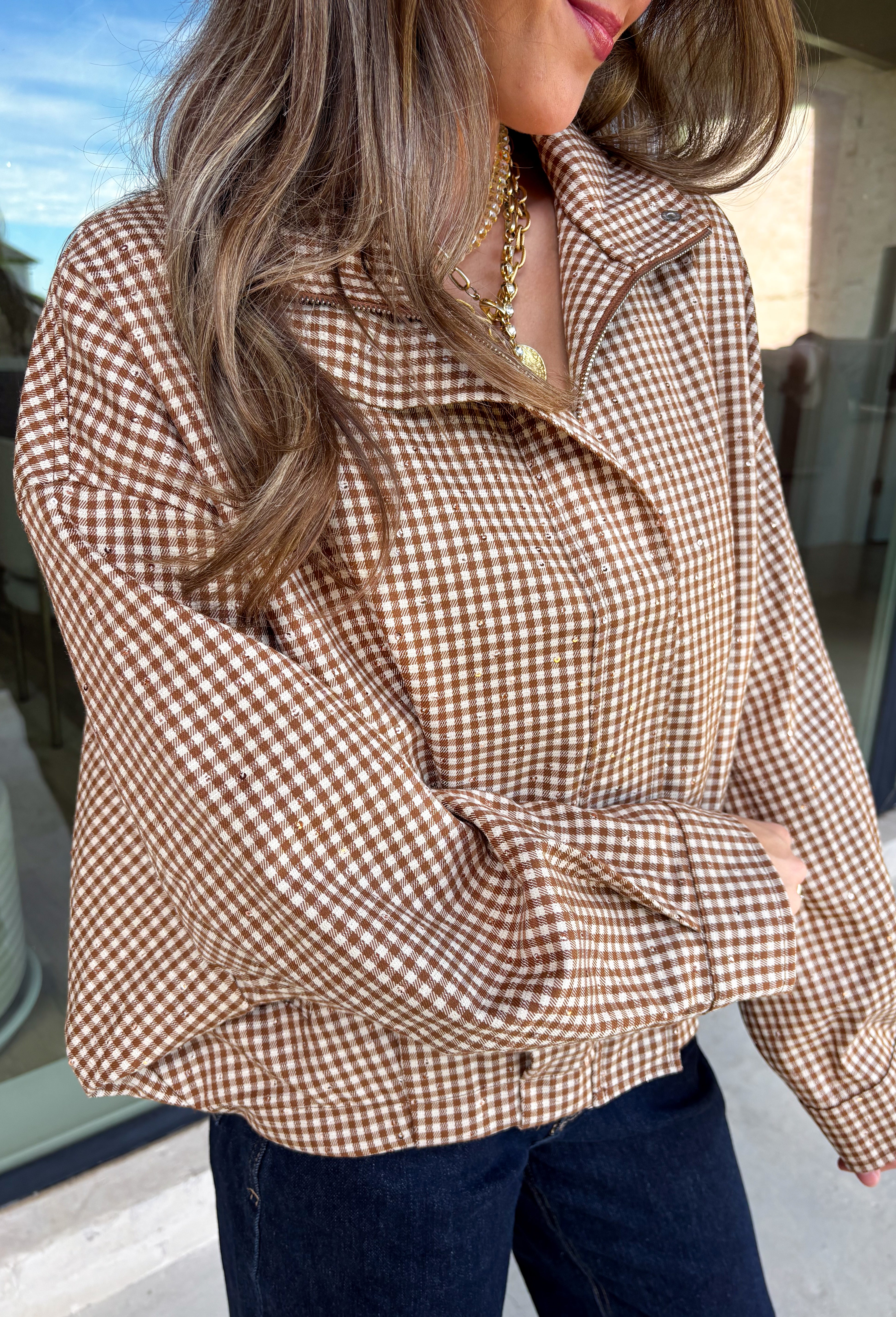 Classic gingham gets a fun fall refresh with this camel and cream jacket from Glam. The neutral checkered print keeps it easy to style, while sequin stitching throughout adds just the right amount of sparkle when it catches the light. A collared neckline and both zipper and button closures give it a structured, jacket-inspired look, while the elastic back hem creates a comfortable shape.