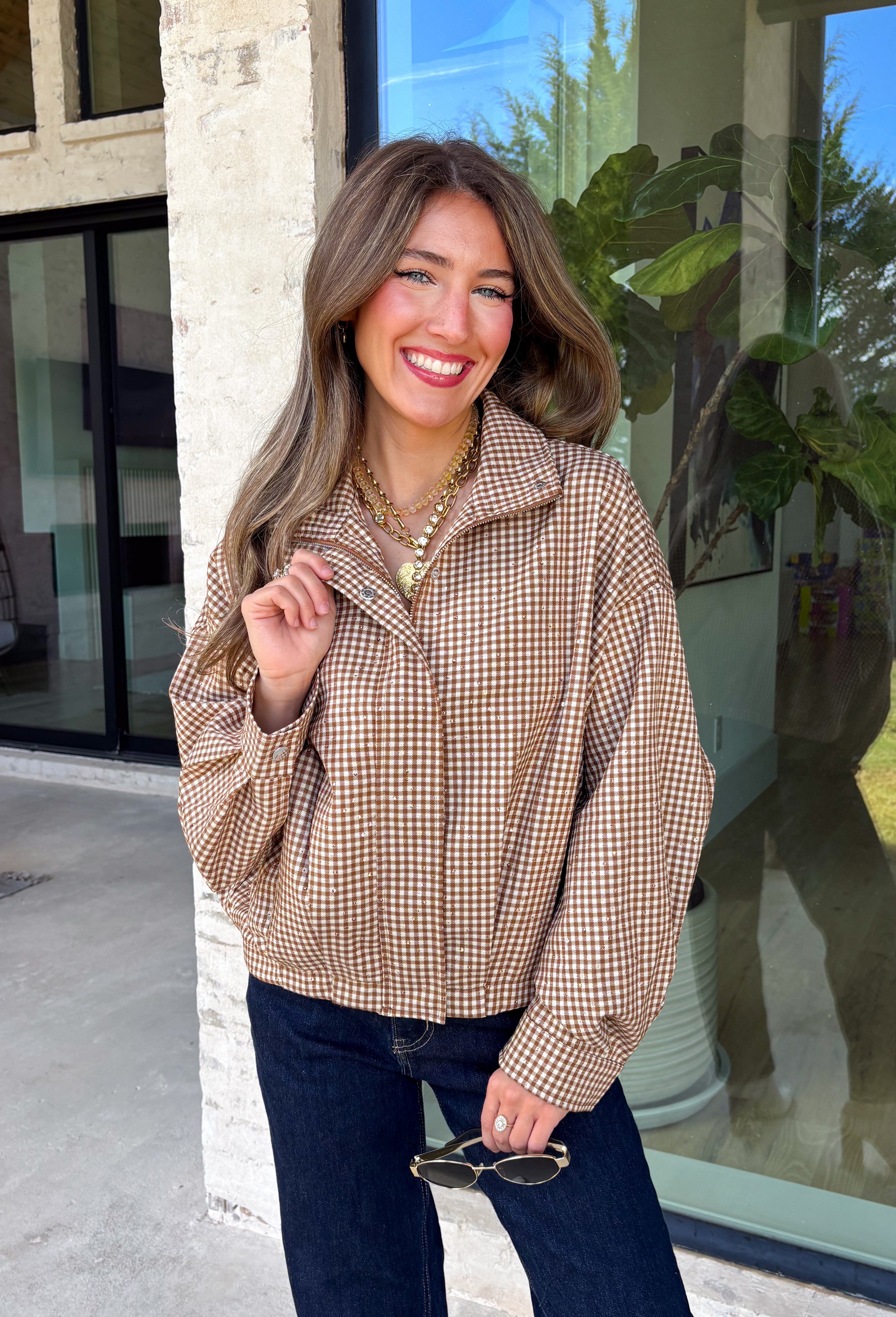 Classic gingham gets a fun fall refresh with this camel and cream jacket from Glam. The neutral checkered print keeps it easy to style, while sequin stitching throughout adds just the right amount of sparkle when it catches the light. A collared neckline and both zipper and button closures give it a structured, jacket-inspired look, while the elastic back hem creates a comfortable shape.