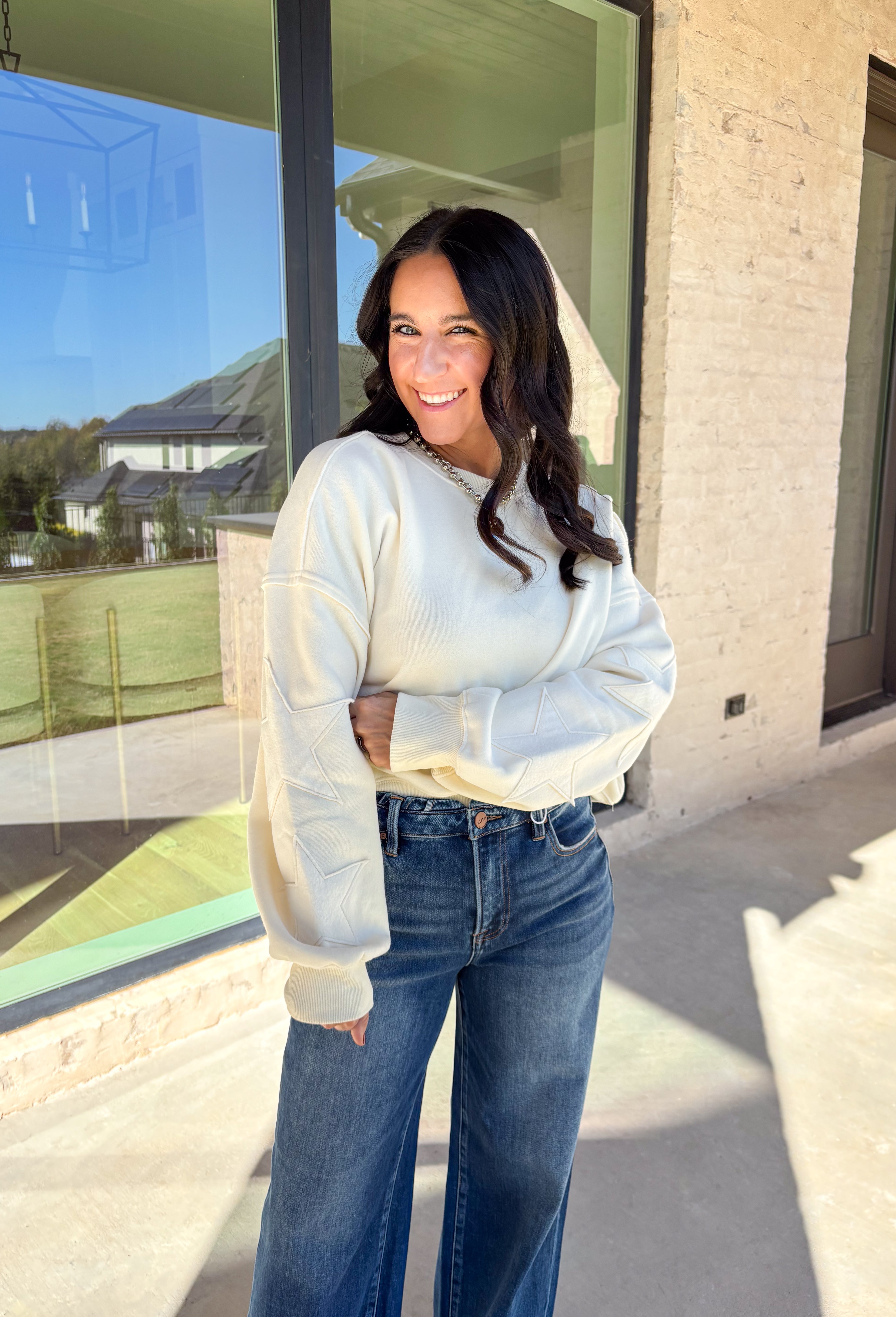 This off-white pullover by Double Zero brings cozy comfort with a touch of playful charm. Featuring two large monochromatic stars on each sleeve, this fleece-lined sweatshirt adds a fun twist to your everyday look. With its relaxed fit and ultra-soft feel, it’s the perfect grab-and-go piece for chilly days or cozy nights in.