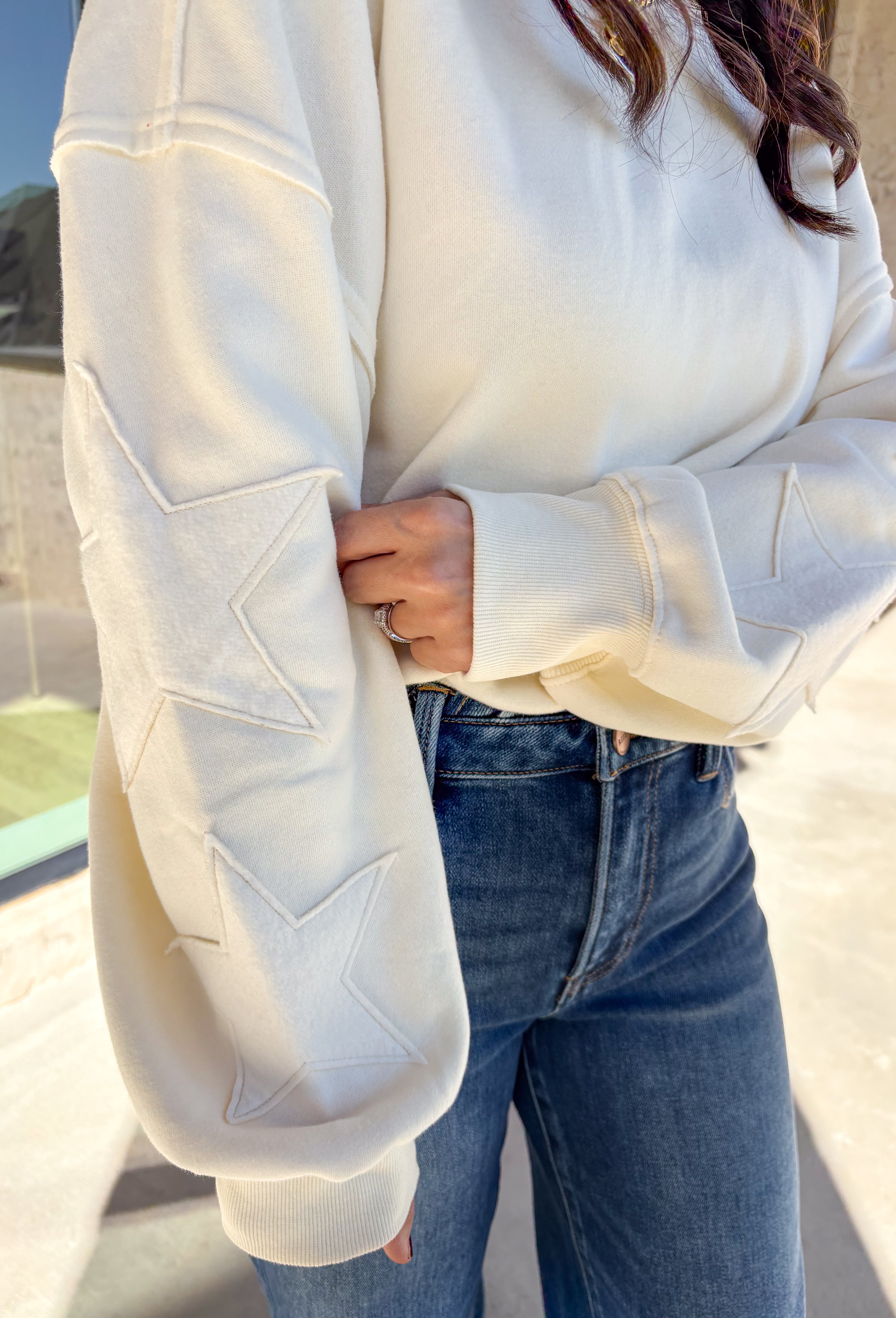 This off-white pullover by Double Zero brings cozy comfort with a touch of playful charm. Featuring two large monochromatic stars on each sleeve, this fleece-lined sweatshirt adds a fun twist to your everyday look. With its relaxed fit and ultra-soft feel, it’s the perfect grab-and-go piece for chilly days or cozy nights in.