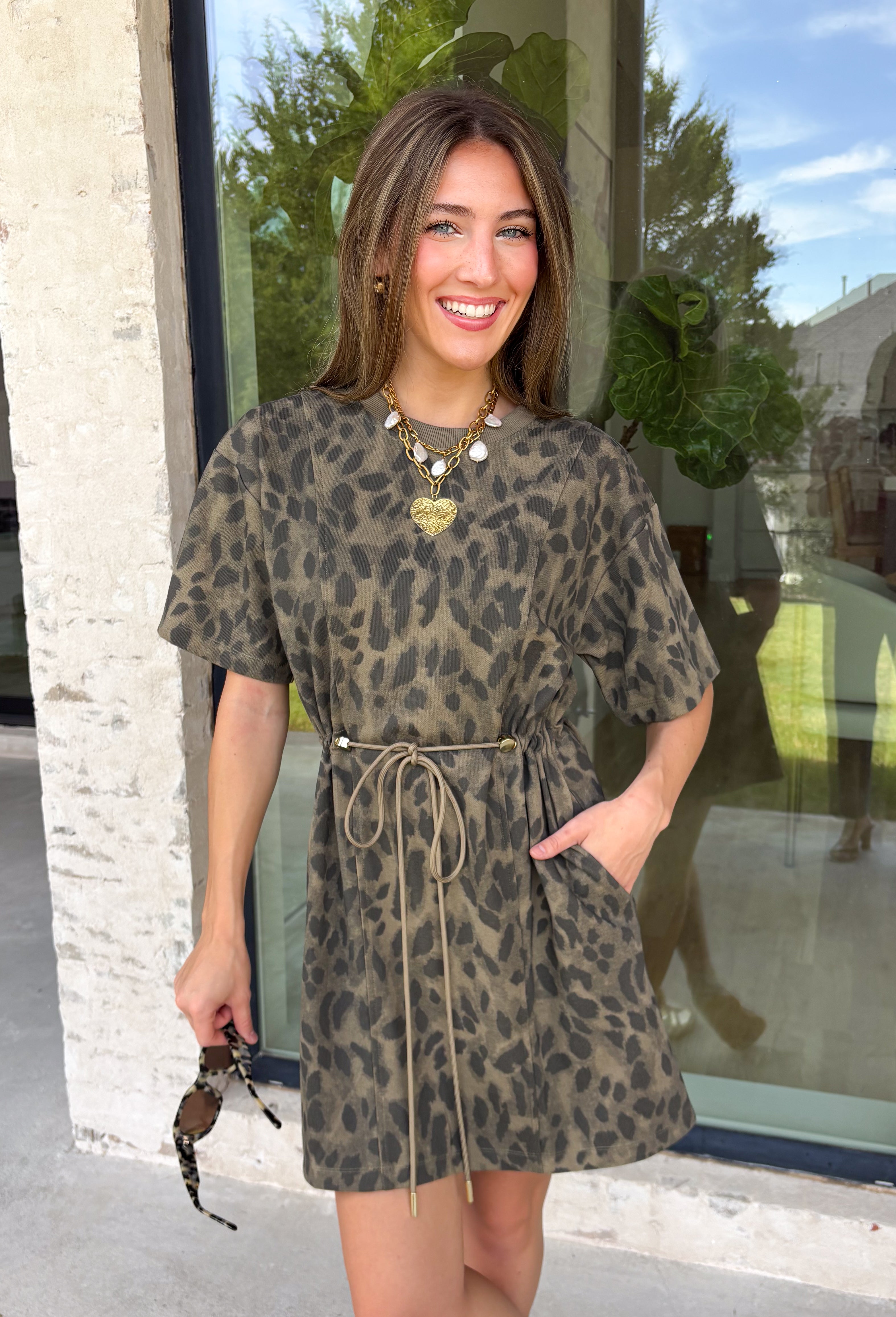 Leopard print is always in style, especially for fall! This olive dress brings together a timeless animal print with an effortlessly flattering silhouette you'll love wearing all season long. The adjustable drawstring waist lets you customize the fit, while the soft fabric keeps it comfortable from morning to night. Finished with short sleeves and everyone's favorite feature—side pockets—this dress is perfect for everything from coffee dates and shopping trips to game days and weekend adventures. 