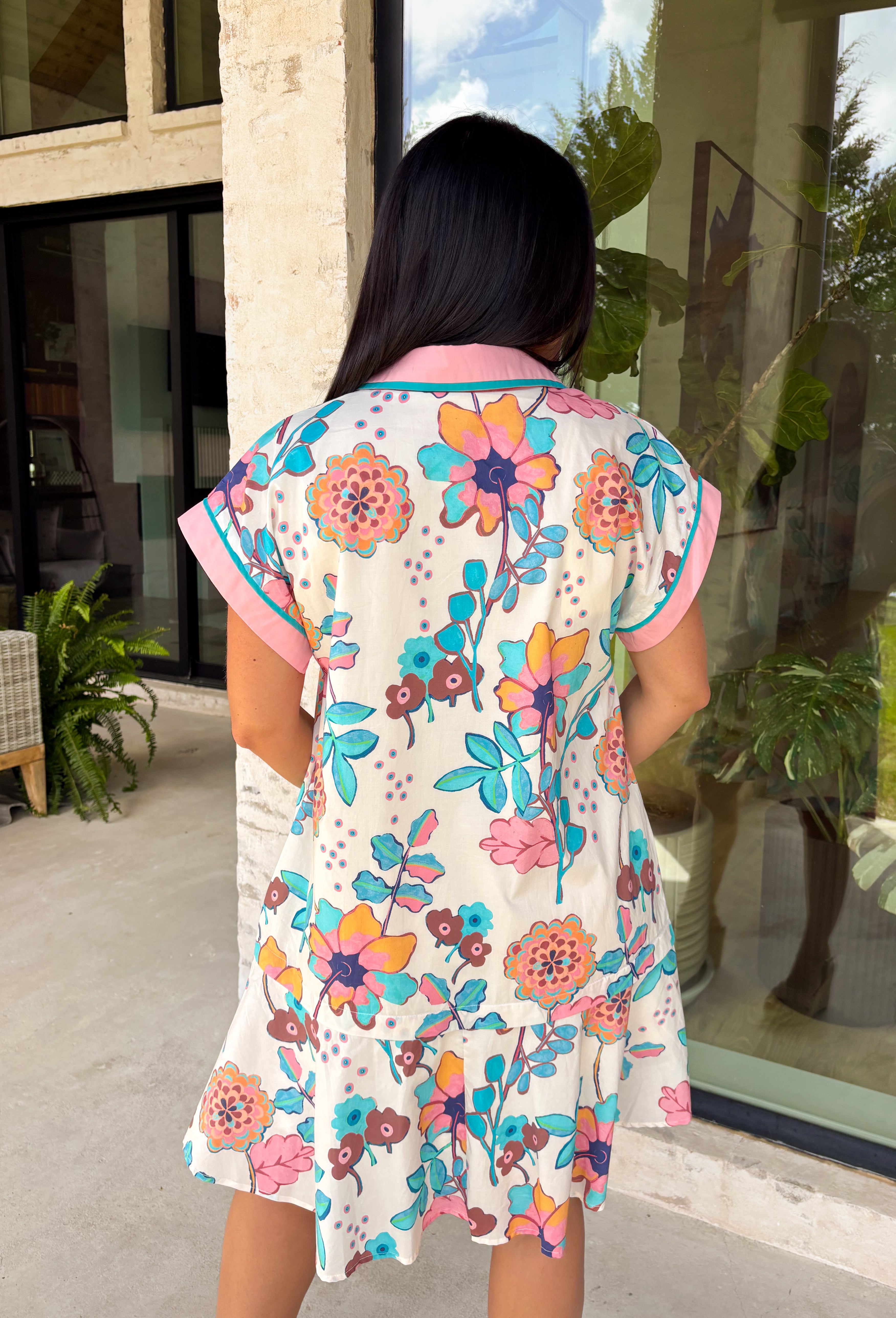 Bright, happy, and made for spring, this off-white short sleeve dress by Entro is bursting with color and charm. Featuring a colorful floral print throughout in shades of coral, blue, pink, and brown, it instantly feels fun and seasonal. The collared neckline adds a classic touch, while the pink and blue trim along the front, neckline, and sleeve cuffs gives it a playful pop of contrast. Fully lined for comfortable wear.