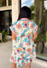 Bright, happy, and made for spring, this off-white short sleeve dress by Entro is bursting with color and charm. Featuring a colorful floral print throughout in shades of coral, blue, pink, and brown, it instantly feels fun and seasonal. The collared neckline adds a classic touch, while the pink and blue trim along the front, neckline, and sleeve cuffs gives it a playful pop of contrast. Fully lined for comfortable wear.