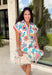 Bright, happy, and made for spring, this off-white short sleeve dress by Entro is bursting with color and charm. Featuring a colorful floral print throughout in shades of coral, blue, pink, and brown, it instantly feels fun and seasonal. The collared neckline adds a classic touch, while the pink and blue trim along the front, neckline, and sleeve cuffs gives it a playful pop of contrast. Fully lined for comfortable wear.