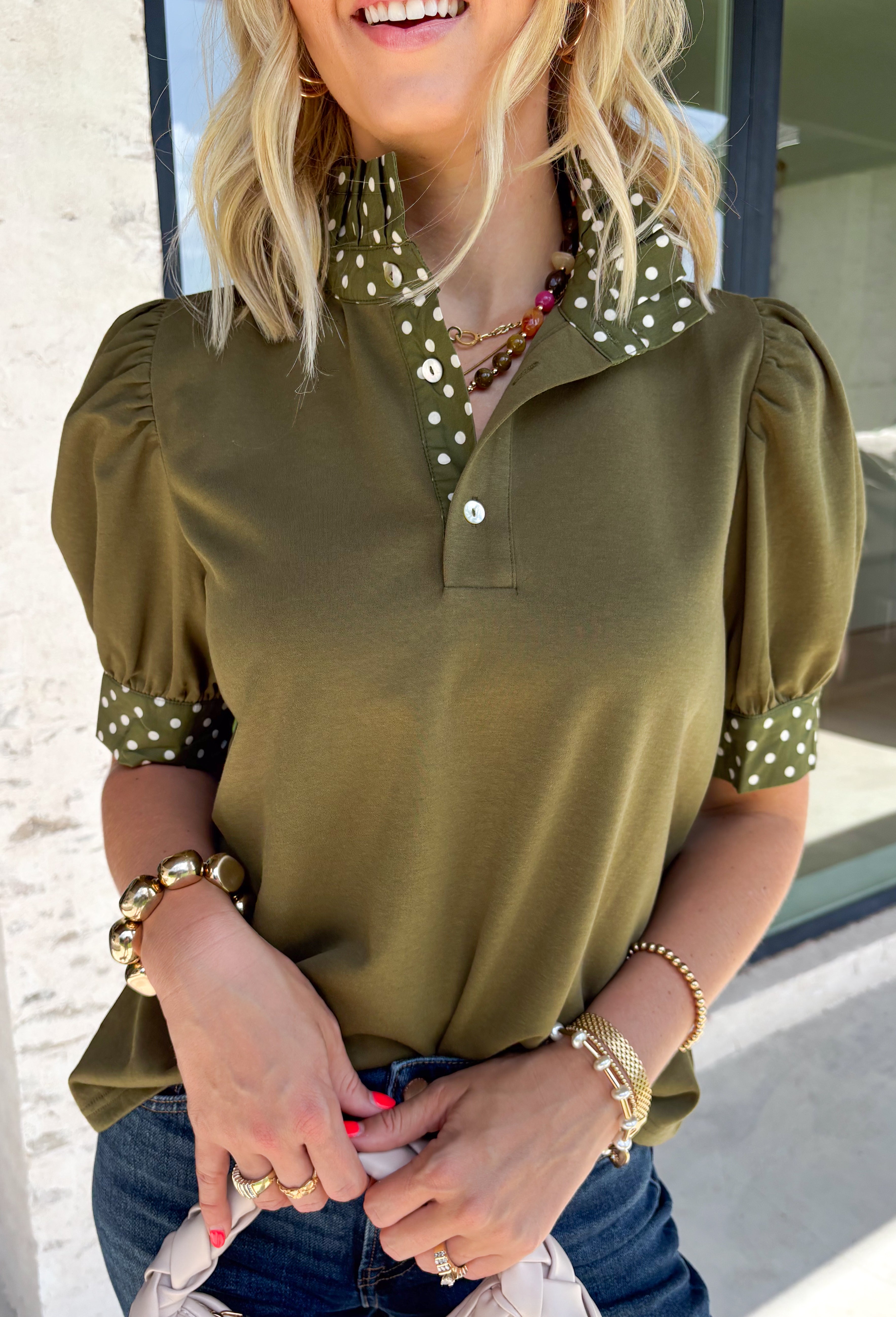 A timeless polka dot print meets feminine details in this effortlessly polished top from Entro. Designed in a rich olive hue with crisp white polka dot accents, this top is perfect for elevating your everyday wardrobe. The ruffled high neckline adds a refined touch, while the button-front closure and contrast cuffs create a beautifully tailored finish. Puff sleeves and button cuffs complete the look, making this versatile blouse an easy choice for everything from workdays to weekend outings.