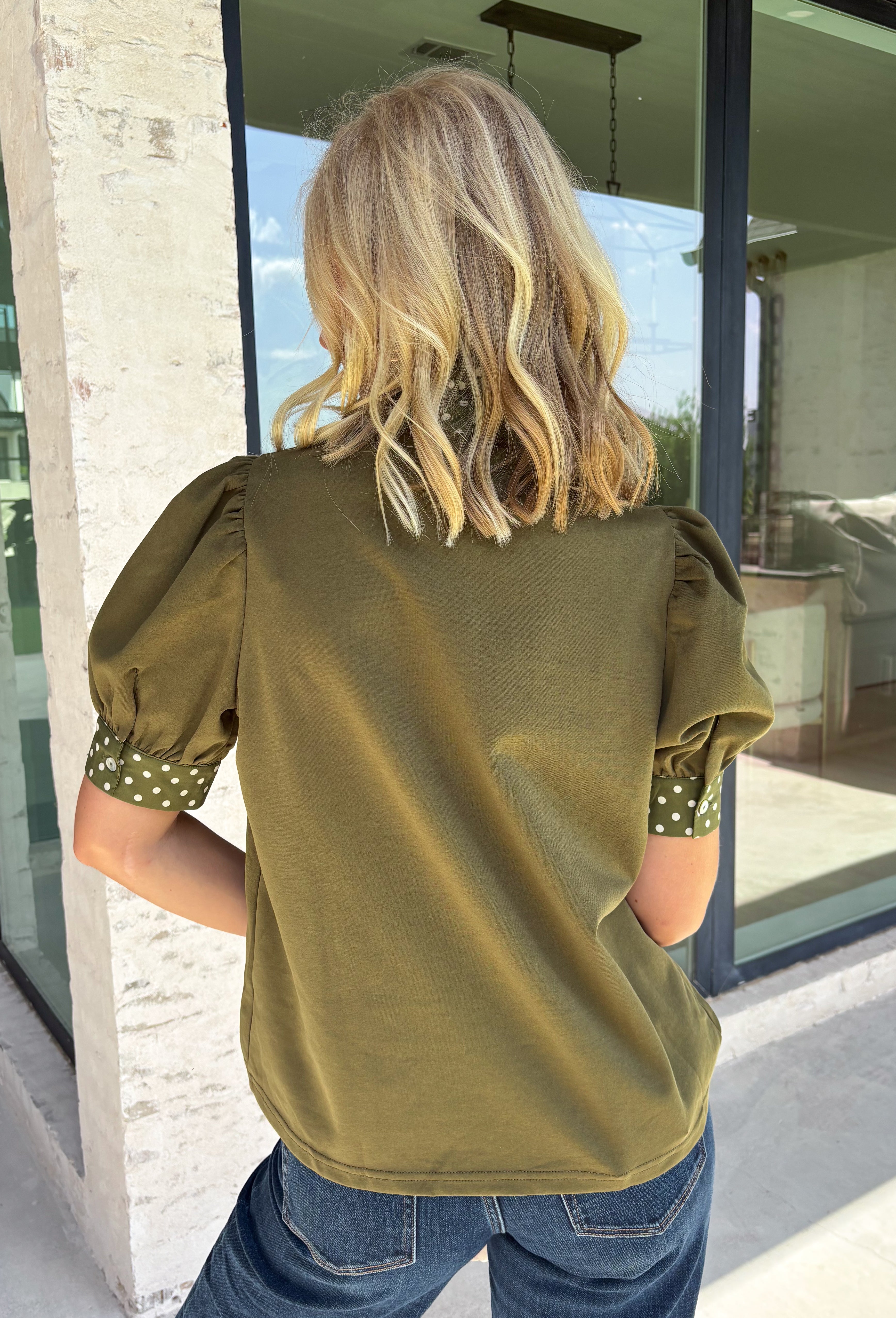A timeless polka dot print meets feminine details in this effortlessly polished top from Entro. Designed in a rich olive hue with crisp white polka dot accents, this top is perfect for elevating your everyday wardrobe. The ruffled high neckline adds a refined touch, while the button-front closure and contrast cuffs create a beautifully tailored finish. Puff sleeves and button cuffs complete the look, making this versatile blouse an easy choice for everything from workdays to weekend outings.