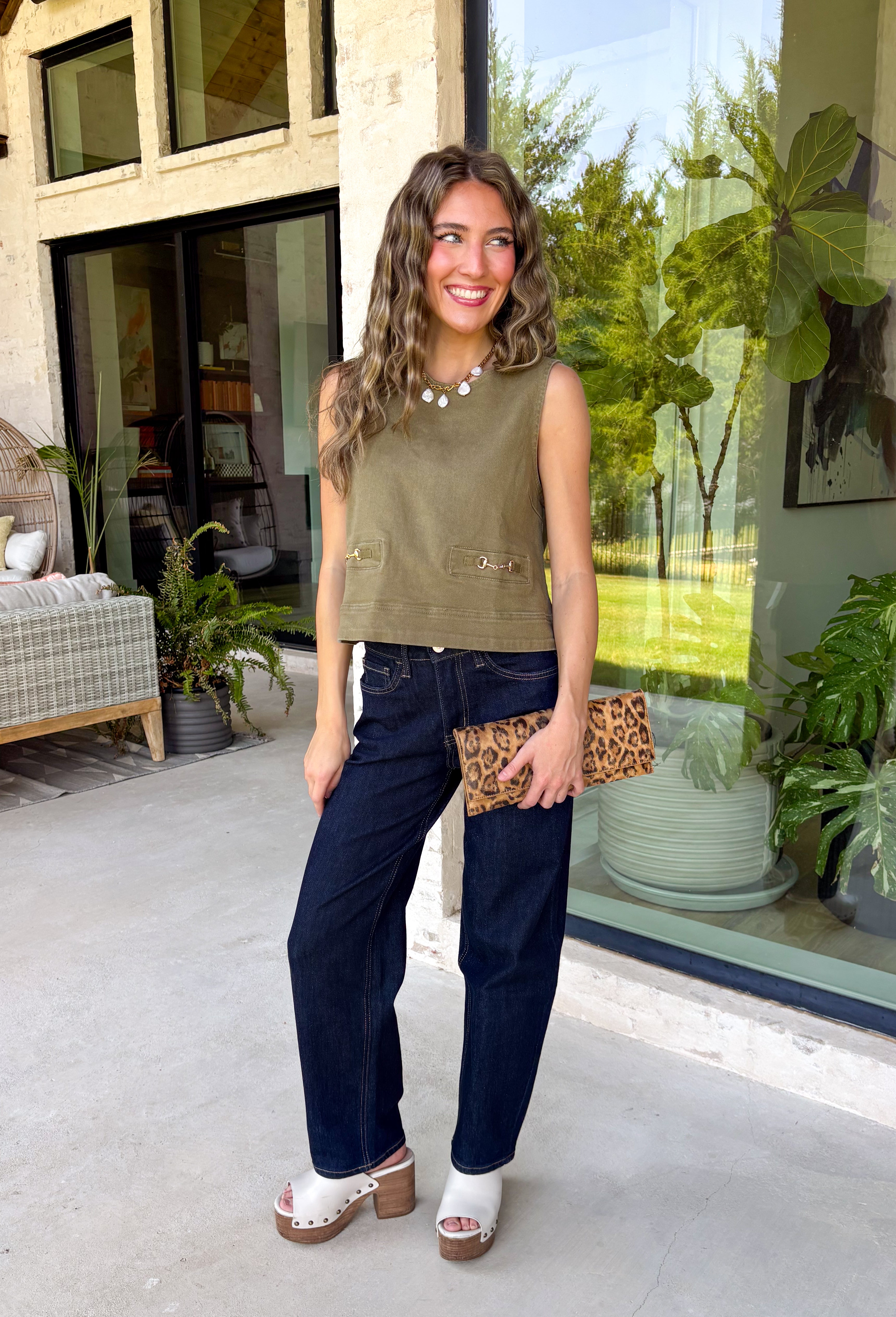 Give your everyday wardrobe a polished update with this effortlessly stylish sleeveless denim top from Entro. Designed in a rich olive denim, this versatile piece features eye-catching gold hardware accent front flap details that add the perfect touch of utility-inspired charm. The clean sleeveless silhouette makes it ideal for layering under jackets and cardigans or wearing on its own.