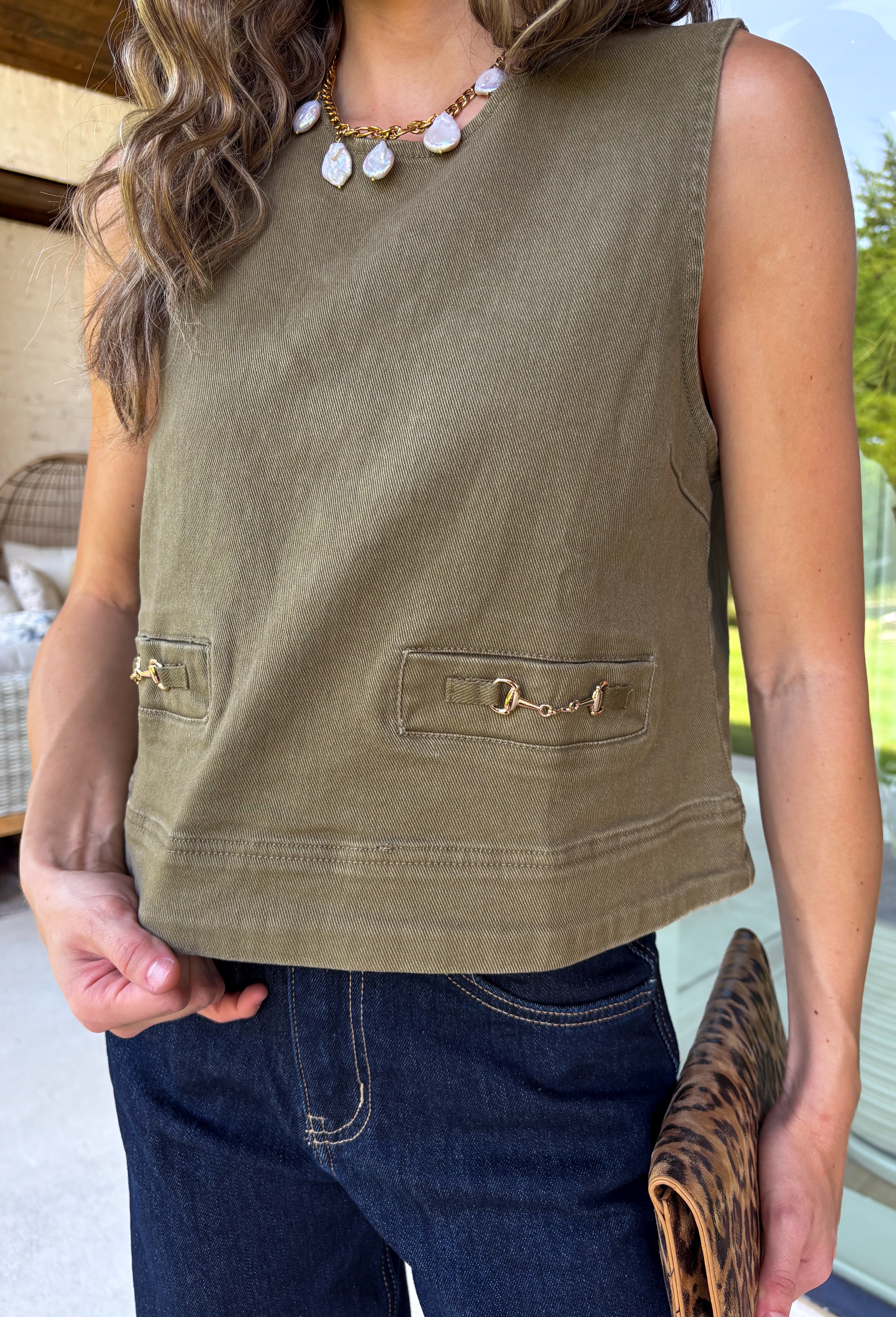 Give your everyday wardrobe a polished update with this effortlessly stylish sleeveless denim top from Entro. Designed in a rich olive denim, this versatile piece features eye-catching gold hardware accent front flap details that add the perfect touch of utility-inspired charm. The clean sleeveless silhouette makes it ideal for layering under jackets and cardigans or wearing on its own.