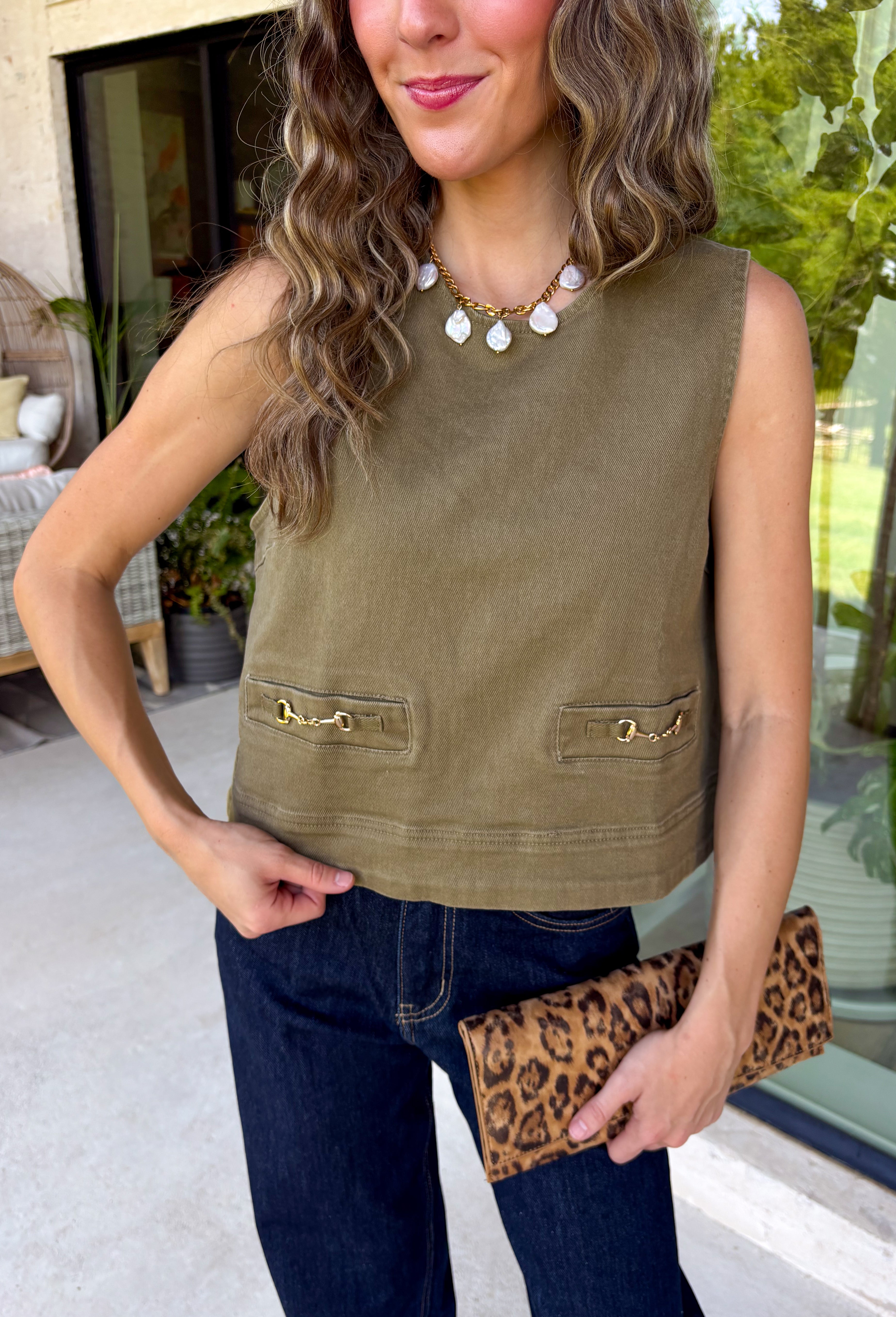Give your everyday wardrobe a polished update with this effortlessly stylish sleeveless denim top from Entro. Designed in a rich olive denim, this versatile piece features eye-catching gold hardware accent front flap details that add the perfect touch of utility-inspired charm. The clean sleeveless silhouette makes it ideal for layering under jackets and cardigans or wearing on its own.