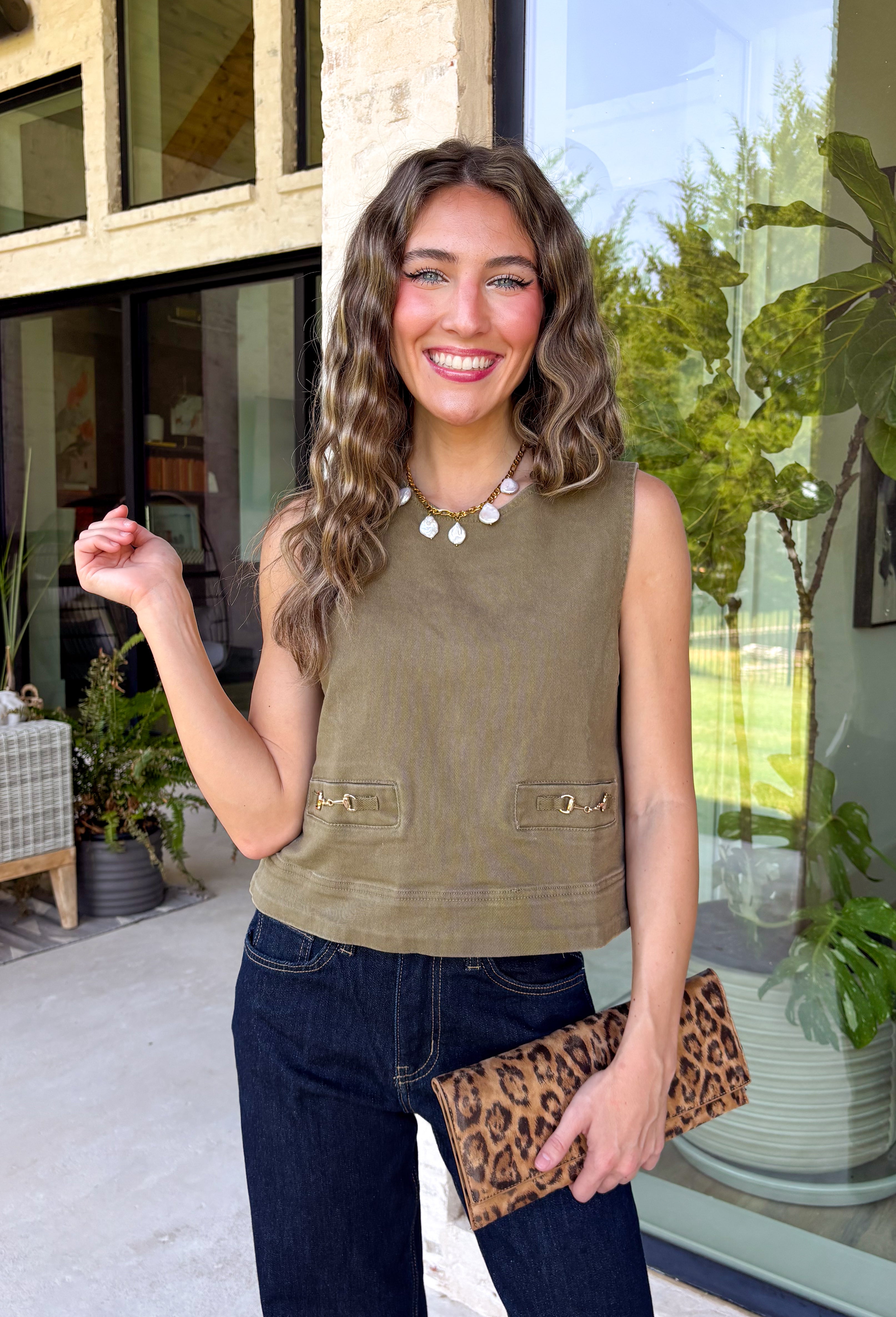 Give your everyday wardrobe a polished update with this effortlessly stylish sleeveless denim top from Entro. Designed in a rich olive denim, this versatile piece features eye-catching gold hardware accent front flap details that add the perfect touch of utility-inspired charm. The clean sleeveless silhouette makes it ideal for layering under jackets and cardigans or wearing on its own.
