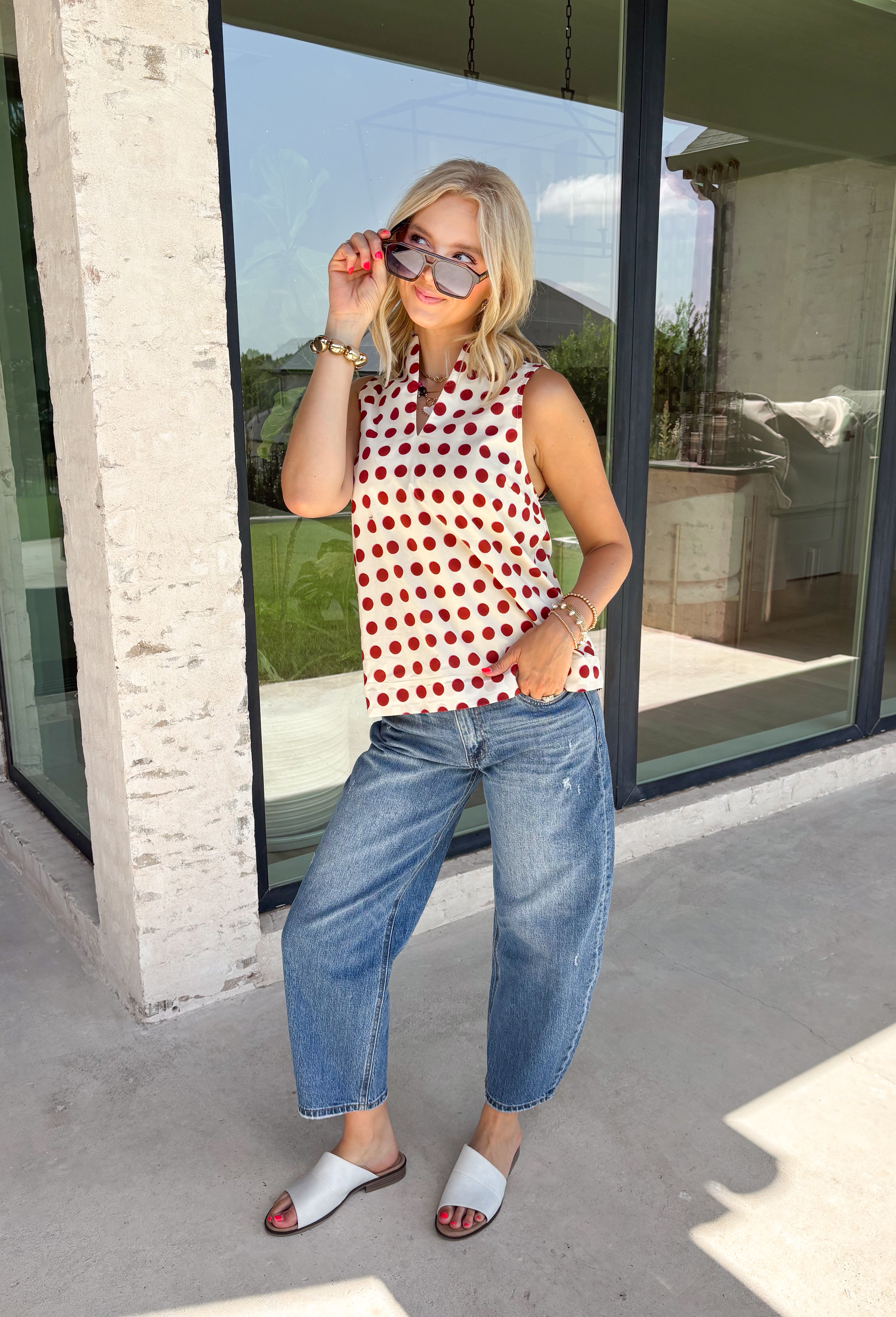 Add a touch of playful charm to your everyday wardrobe with this effortlessly polished sleeveless top from Entro. Featuring a soft ecru backdrop with a rust polka dot print and subtle pops of pink, this lightweight blouse is full of warm seasonal color. The flattering v-neckline keeps the look timeless, while the pleated back detail adds beautiful movement and an easy, flowy fit. 