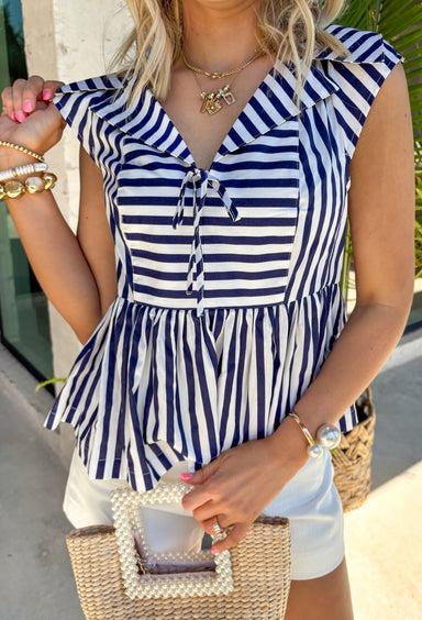 Nothing says effortless spring style quite like navy and white stripes. This classic collared top by Fate gets a fresh update with a flattering front tie detail that adds just the right touch of charm. Crisp yet relaxed, it’s the kind of piece you’ll reach for on sunny mornings, weekend brunch dates, and everything in between. Lightweight and breathable in 100% cotton, this striped beauty pairs perfectly with white denim, cutoffs, or your favorite wide-leg jeans for that easy coastal-inspired look.