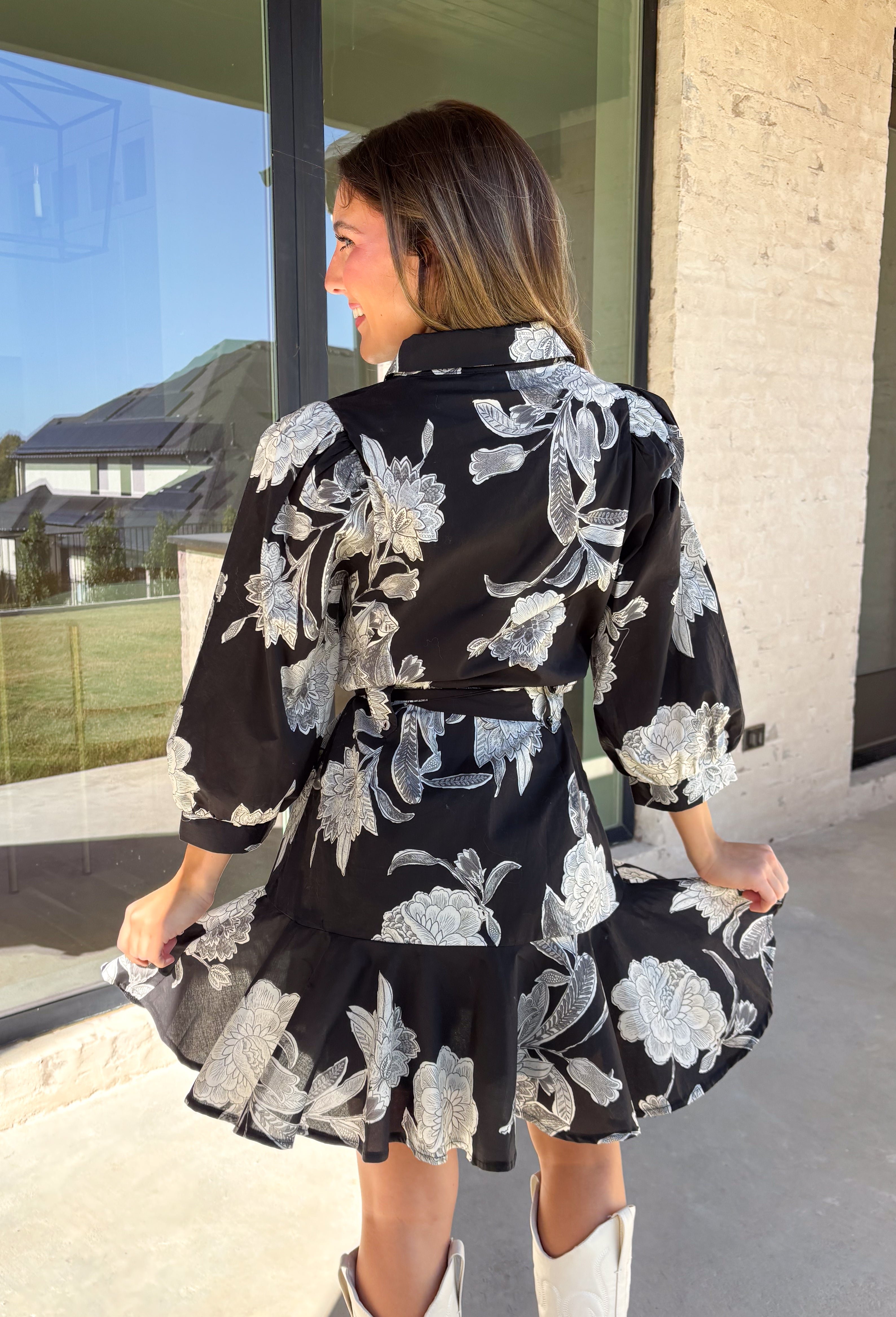 This black floral dress by Entro is a timeless favorite with a touch of charm. Designed with an off-white and gray floral print, it features ¾ puff sleeves, a button-front closure, and a flattering self-tie waist belt. The chest pocket adds a subtle utility touch, while the tiered ruffle hem and side pockets keep the look feminine and functional. This dress is perfect for any special occasion!
