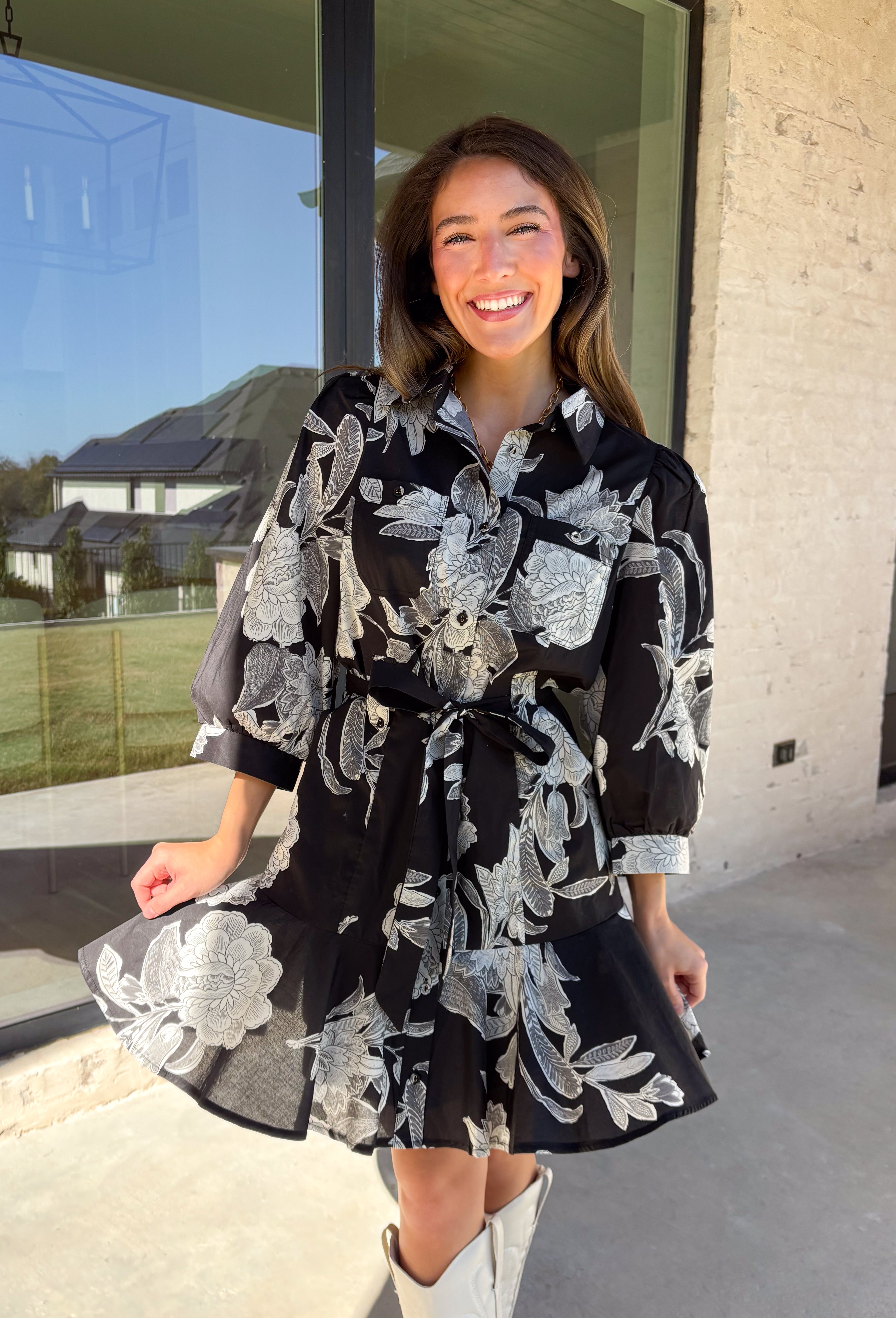This black floral dress by Entro is a timeless favorite with a touch of charm. Designed with an off-white and gray floral print, it features ¾ puff sleeves, a button-front closure, and a flattering self-tie waist belt. The chest pocket adds a subtle utility touch, while the tiered ruffle hem and side pockets keep the look feminine and functional. This dress is perfect for any special occasion!