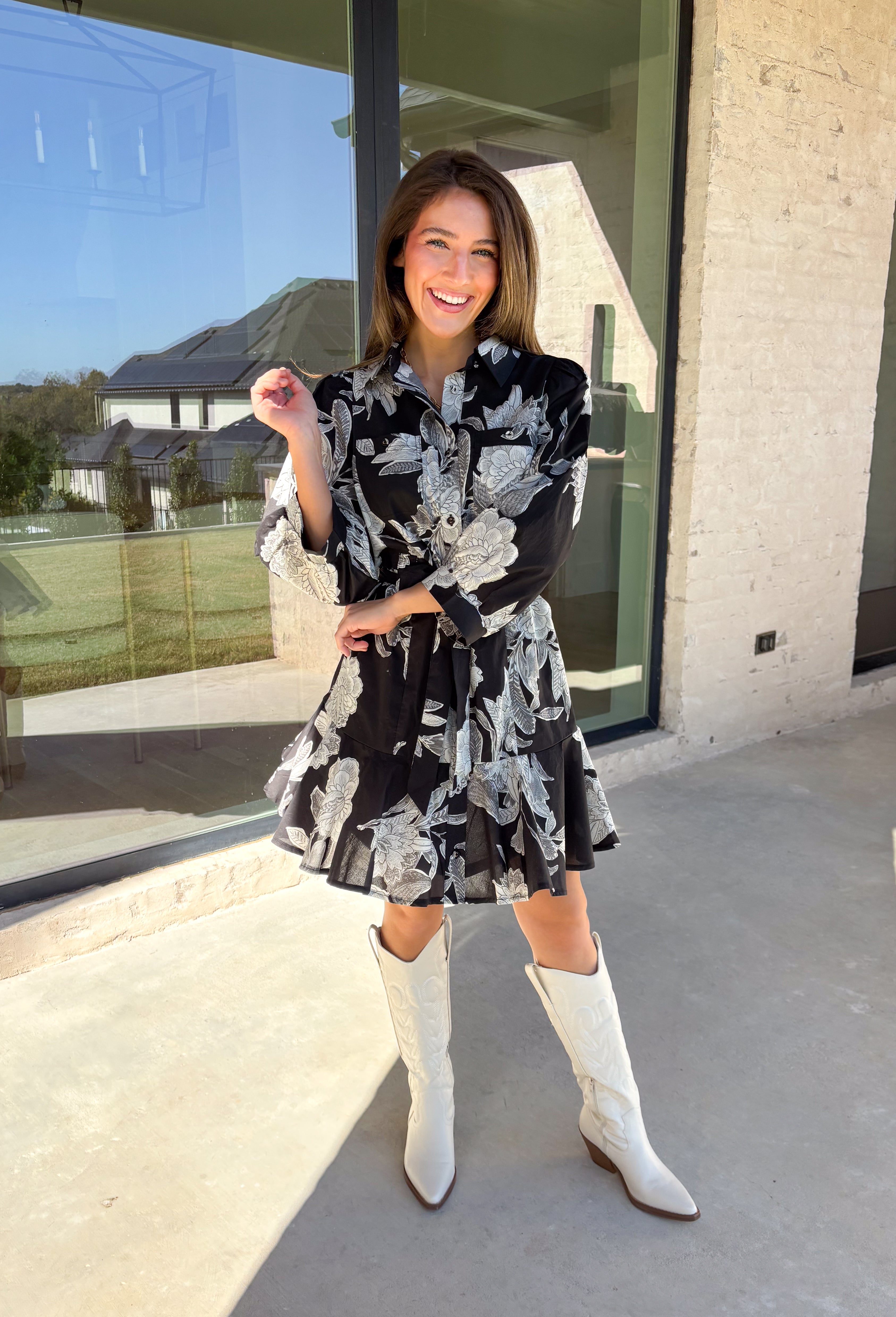 This black floral dress by Entro is a timeless favorite with a touch of charm. Designed with an off-white and gray floral print, it features ¾ puff sleeves, a button-front closure, and a flattering self-tie waist belt. The chest pocket adds a subtle utility touch, while the tiered ruffle hem and side pockets keep the look feminine and functional. This dress is perfect for any special occasion!