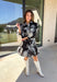 This black floral dress by Entro is a timeless favorite with a touch of charm. Designed with an off-white and gray floral print, it features ¾ puff sleeves, a button-front closure, and a flattering self-tie waist belt. The chest pocket adds a subtle utility touch, while the tiered ruffle hem and side pockets keep the look feminine and functional. This dress is perfect for any special occasion!