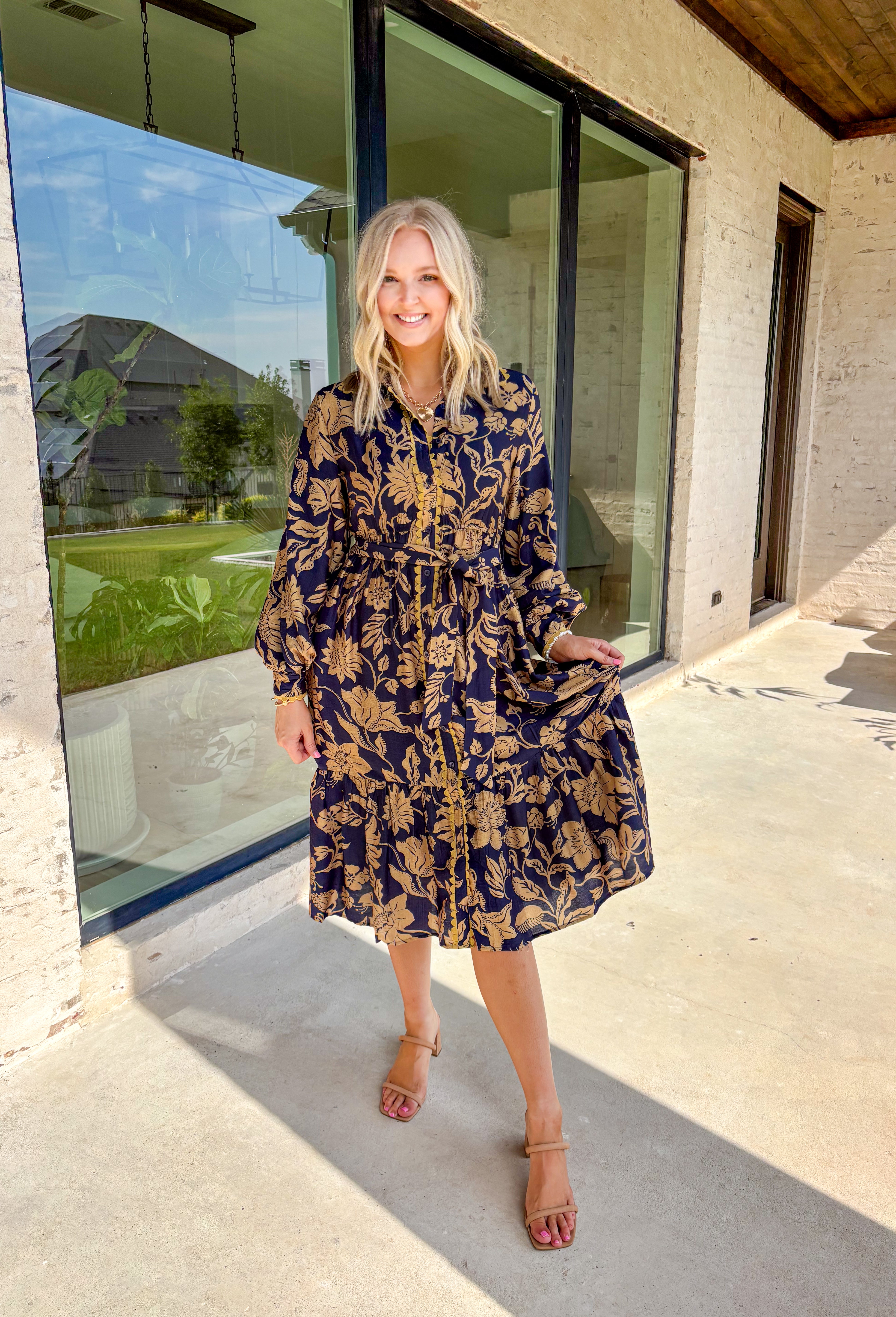 Moody florals meet timeless tailoring in this navy midi dress, patterned with an olive abstract floral print that’s perfect for fall. Scalloped trim along the front softens the look, while the collared neckline and button-down design keep it classic. Balloon sleeves add a hint of drama, and the self-tie waist lets you create a flattering, adjustable fit. Finished with a midi length for versatile styling, this piece is just as ready for weekday wear as it is for weekend outings.