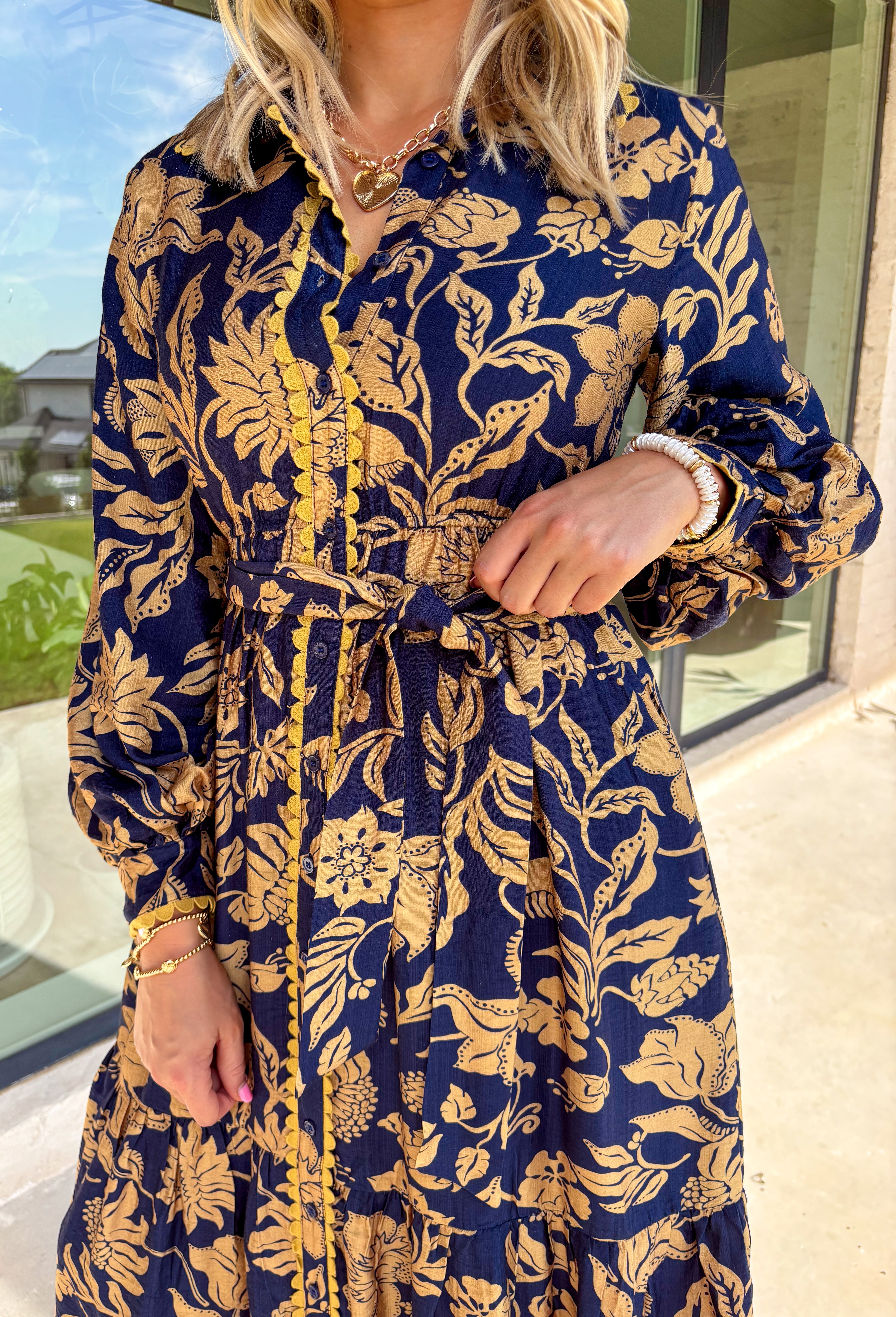 Moody florals meet timeless tailoring in this navy midi dress, patterned with an olive abstract floral print that’s perfect for fall. Scalloped trim along the front softens the look, while the collared neckline and button-down design keep it classic. Balloon sleeves add a hint of drama, and the self-tie waist lets you create a flattering, adjustable fit. Finished with a midi length for versatile styling, this piece is just as ready for weekday wear as it is for weekend outings.