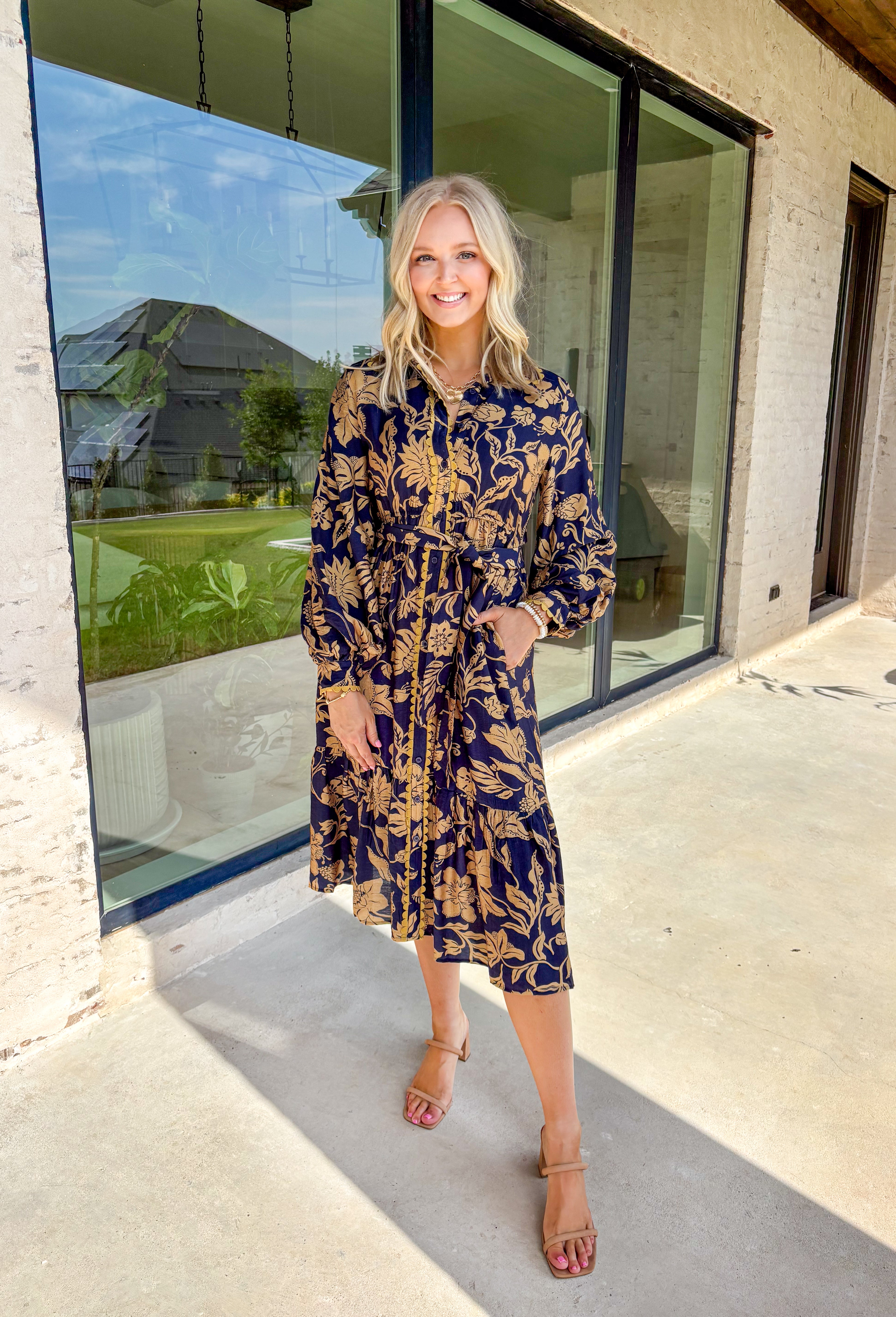 Moody florals meet timeless tailoring in this navy midi dress, patterned with an olive abstract floral print that’s perfect for fall. Scalloped trim along the front softens the look, while the collared neckline and button-down design keep it classic. Balloon sleeves add a hint of drama, and the self-tie waist lets you create a flattering, adjustable fit. Finished with a midi length for versatile styling, this piece is just as ready for weekday wear as it is for weekend outings.