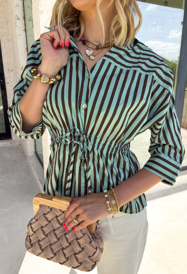 Fresh colors and flattering details make this striped blouse an easy favorite for the season. Designed with soft mint and brown stripes, this effortlessly polished top features a classic v-neckline and button-front design for timeless appeal. The adjustable drawstring waist creates a flattering, customizable fit, while the ¾-length sleeves with button cuffs add a refined finishing touch. Crafted from breathable cotton, this versatile blouse transitions seamlessly from workdays to weekend outings.