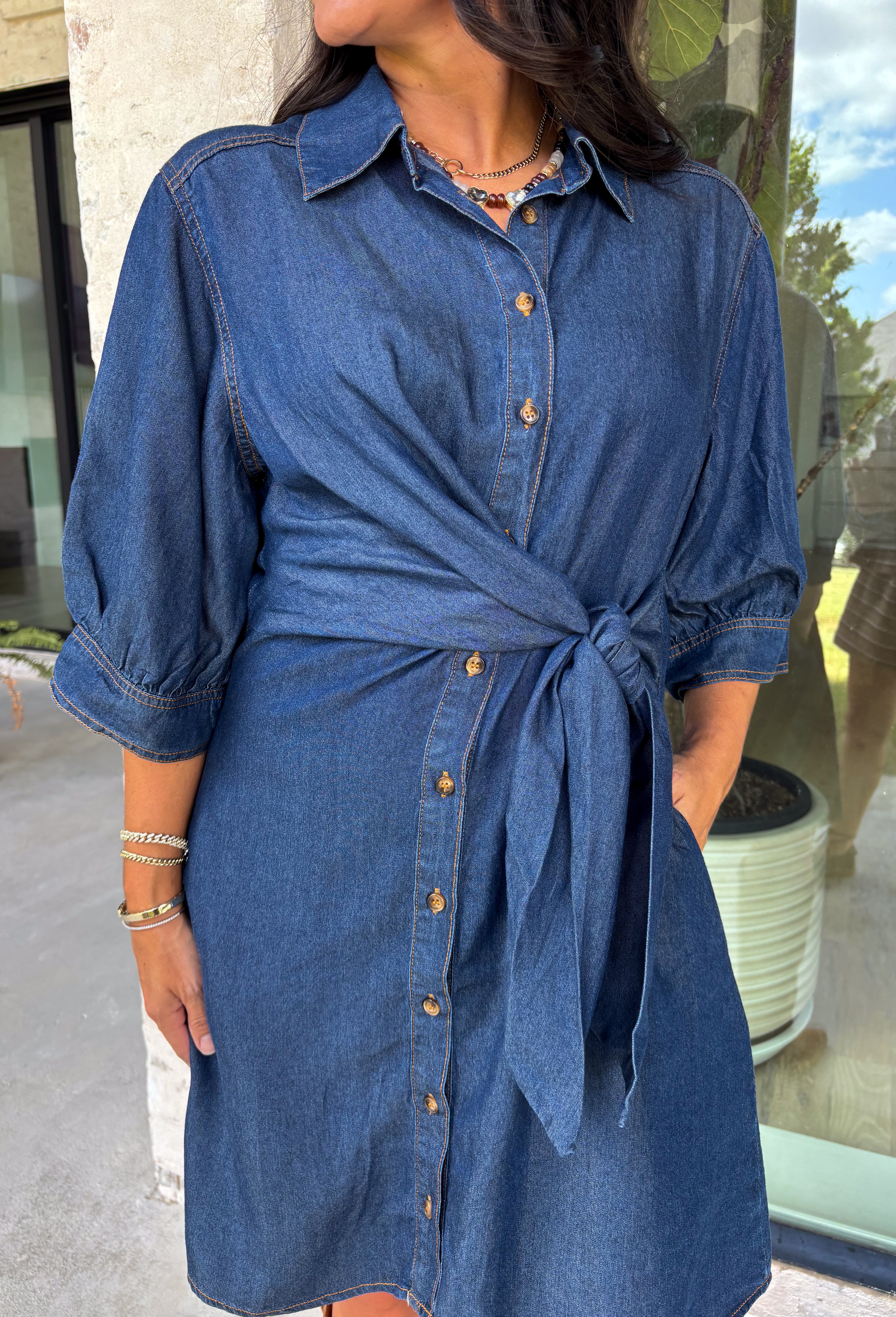 A timeless denim dress is always in style, and this lightweight beauty from Entro is one you'll wear on repeat. Crafted from soft medium wash tencel denim, this effortlessly flattering dress features a classic button-front design, a feminine v-neckline, and a matching self-tie waist that creates the perfect customizable fit. The ¾ length sleeves with button cuffs add a polished touch, while side pockets make it as practical as it is stylish. 