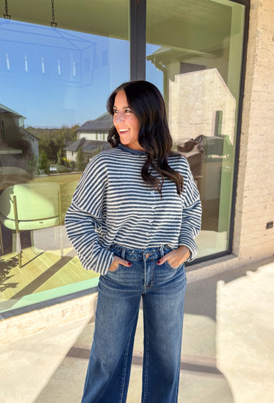 Classic stripes meet cozy comfort in this navy and white button-down cardigan by Things Between. Designed in a soft knit with a relaxed fit, this timeless piece brings effortless warmth to your winter wardrobe. The simple stripe pattern adds a touch of everyday charm, making it easy to style for layering through the colder months.