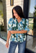Bring a fresh take on fall florals to your wardrobe with this beautiful hunter green top. Featuring a delicate blue and off white floral print, this timeless top is perfect for everything from office days to weekend outings. The pintuck detailing along the front adds an elevated touch, while the button front and short puff sleeves create a feminine silhouette you'll love season after season. 