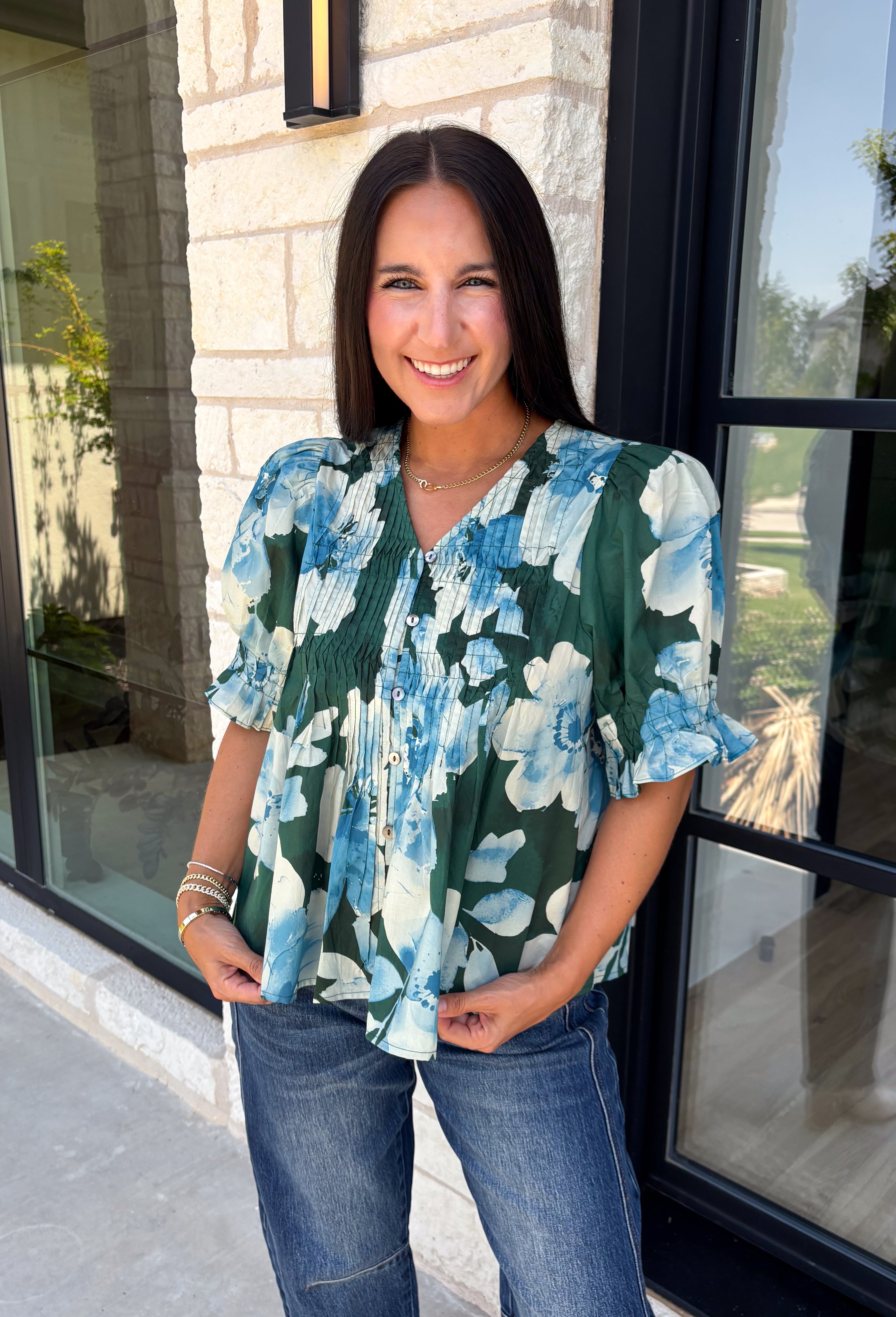 Bring a fresh take on fall florals to your wardrobe with this beautiful hunter green top. Featuring a delicate blue and off white floral print, this timeless top is perfect for everything from office days to weekend outings. The pintuck detailing along the front adds an elevated touch, while the button front and short puff sleeves create a feminine silhouette you'll love season after season. 