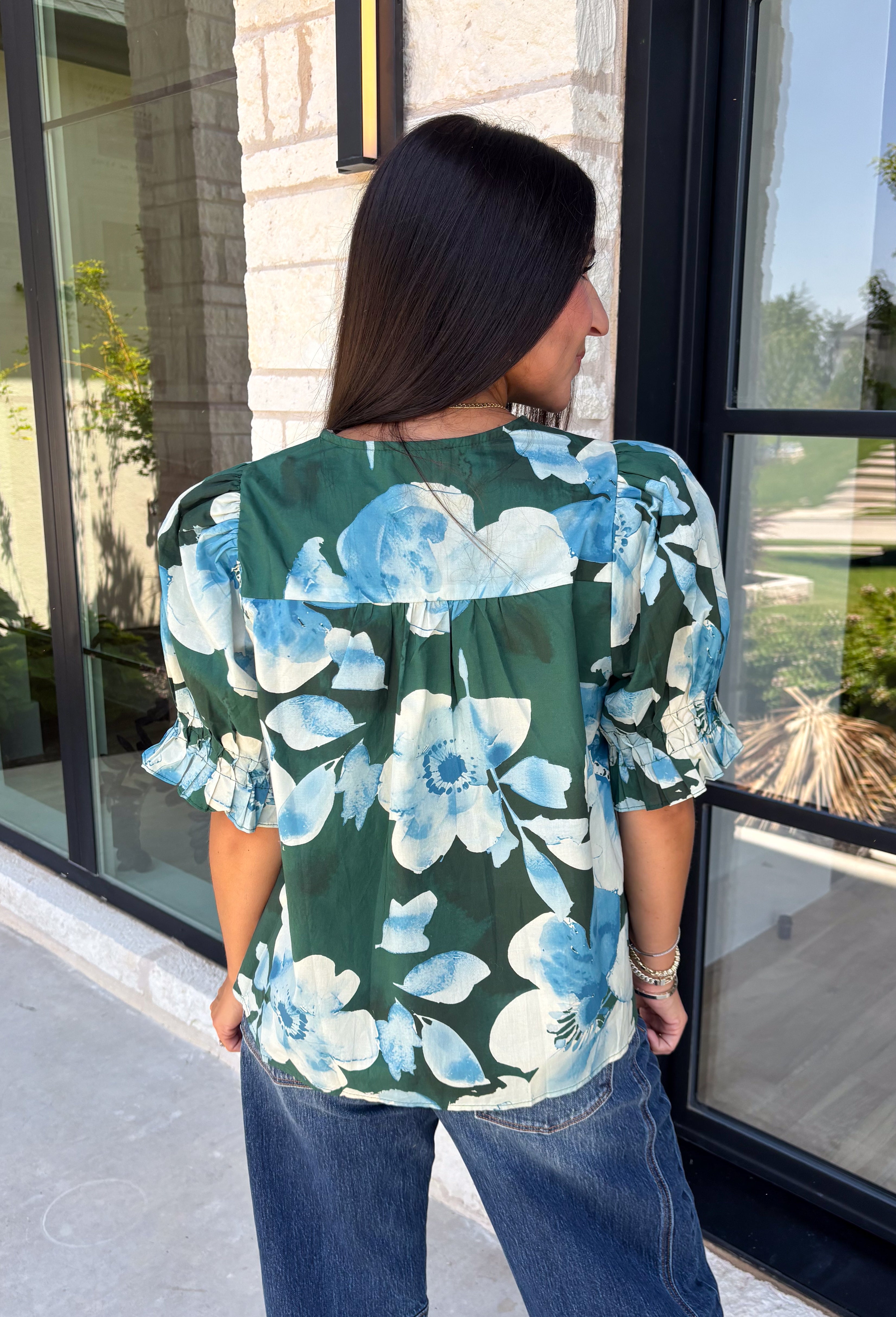 Bring a fresh take on fall florals to your wardrobe with this beautiful hunter green top. Featuring a delicate blue and off white floral print, this timeless top is perfect for everything from office days to weekend outings. The pintuck detailing along the front adds an elevated touch, while the button front and short puff sleeves create a feminine silhouette you'll love season after season. 