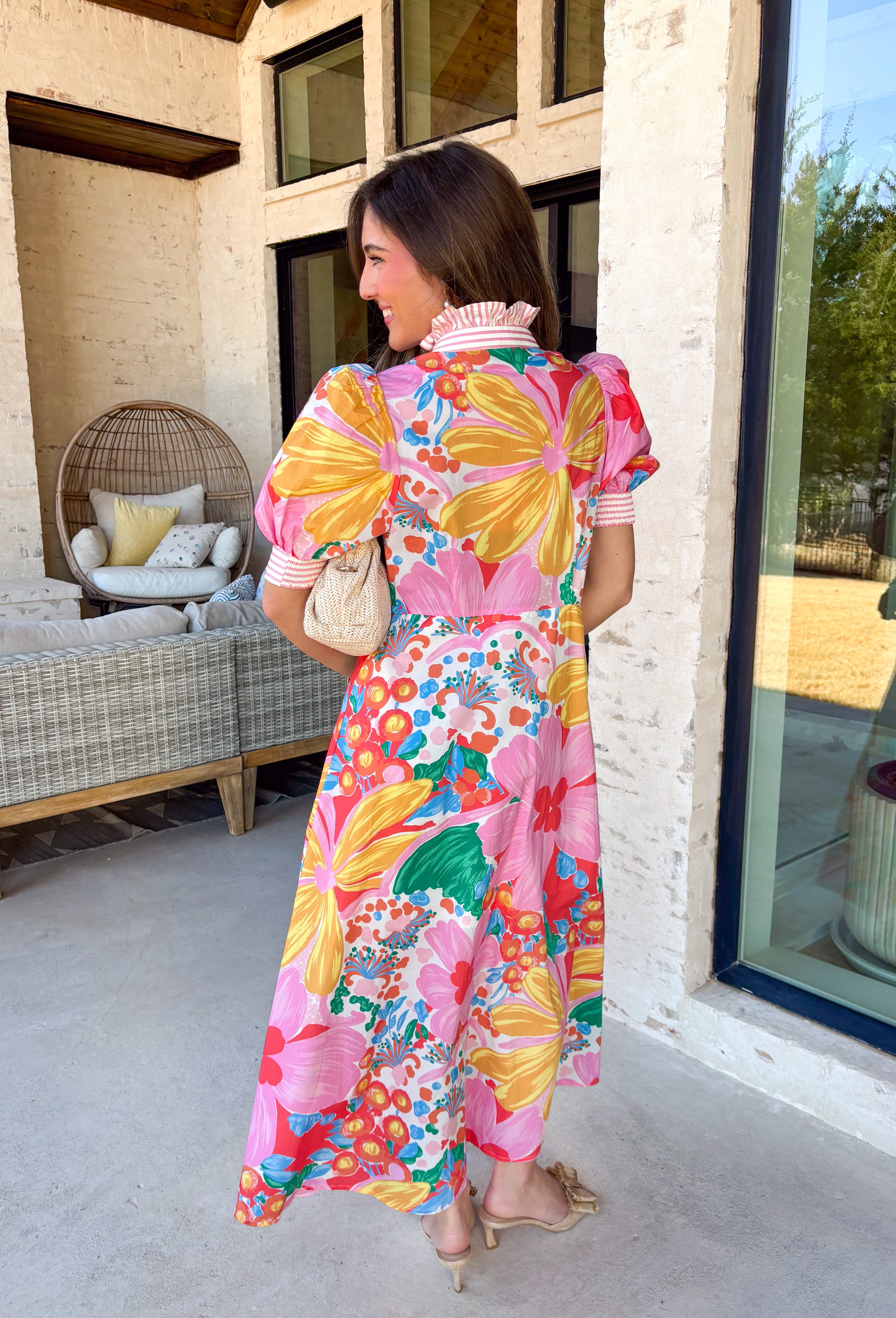 Bright, joyful, and bursting with spring color, this white short sleeve button-down dress by Entro is a total showstopper. Featuring a bold floral print in pink, red, blue, yellow, green, and orange, it brings instant happy vibes to your wardrobe. The ruffle neckline is trimmed with pink and white stripes for a fun pop of contrast, with matching stripe detail running down the front and along the sleeve cuffs. Smocking at the back of the sleeves adds comfort and shape, while side pockets and a lining make it