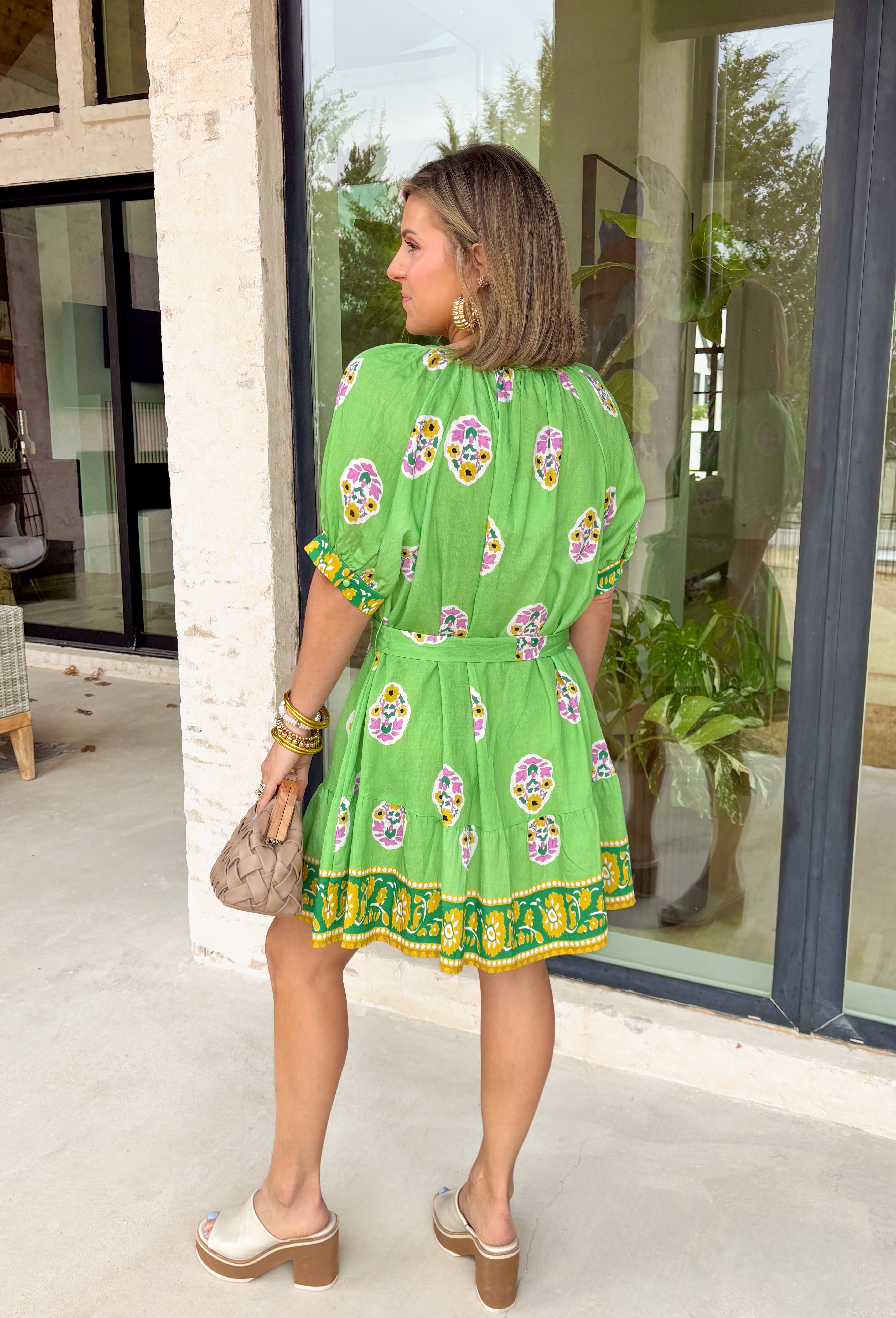 Bring a burst of sunshine to your spring wardrobe with this lime green dress. The lively floral print features playful pops of lilac, green, and white, while the contrasting hem in green, mustard, and white adds a fun, unexpected twist. The button-down front and self-tie belt create a flattering, adjustable fit, and the lightweight fabric keeps it breezy for warm spring days. Whether you’re headed to brunch or strolling the farmers’ market, this dress is all about easy, cheerful style.