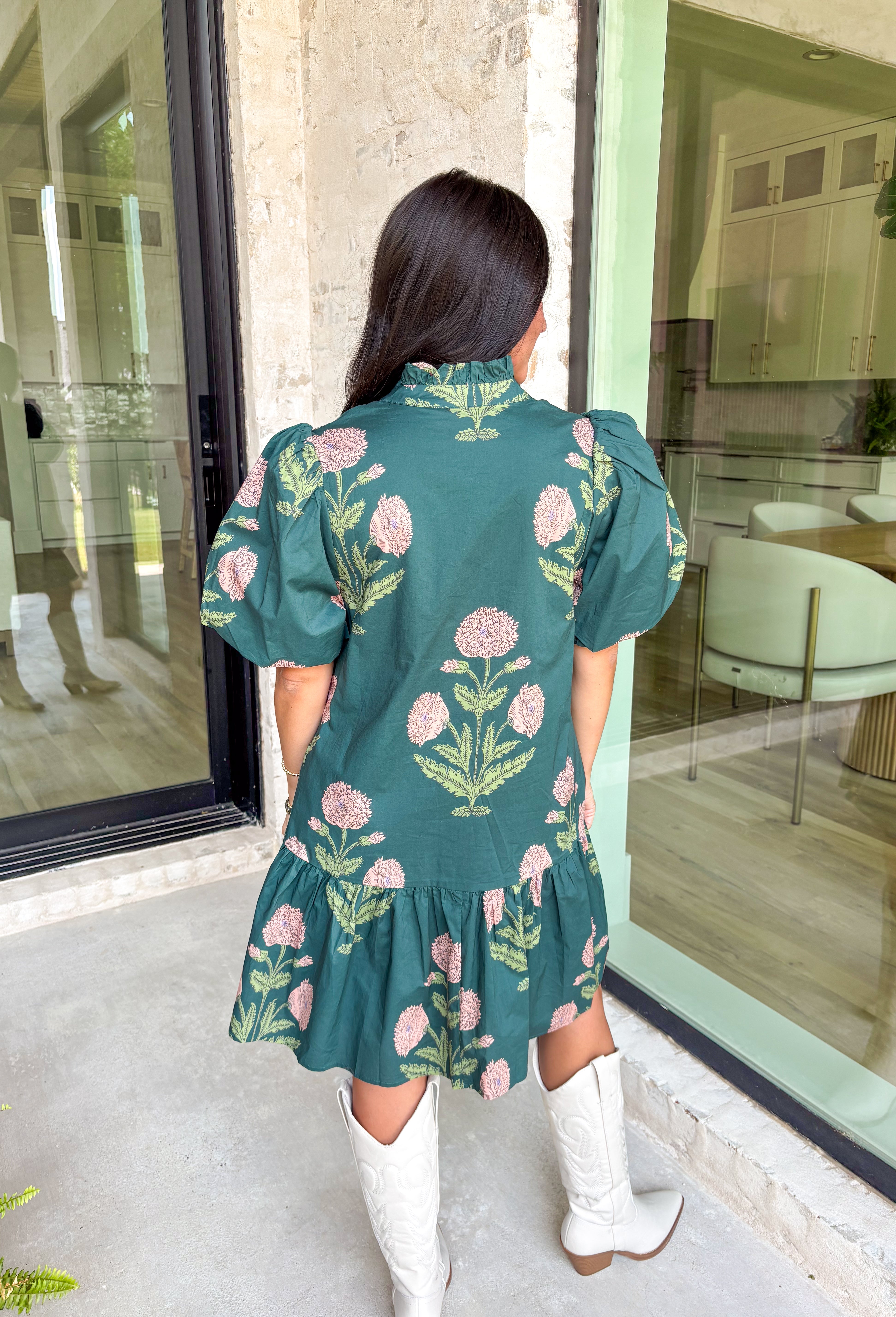 Rich, romantic, and made for fall days, this hunter green mini dress is covered in a warm seasonal floral print. The ruffle neck band collar with gold accent button closure adds a polished touch, while the short bubble sleeves and flouncy ruffle hem keep it playful and feminine. Side pockets bring in that practical detail we love, and the fully lined cotton design makes it comfortable from day to night. Perfect for everything from brunch to seasonal gatherings.