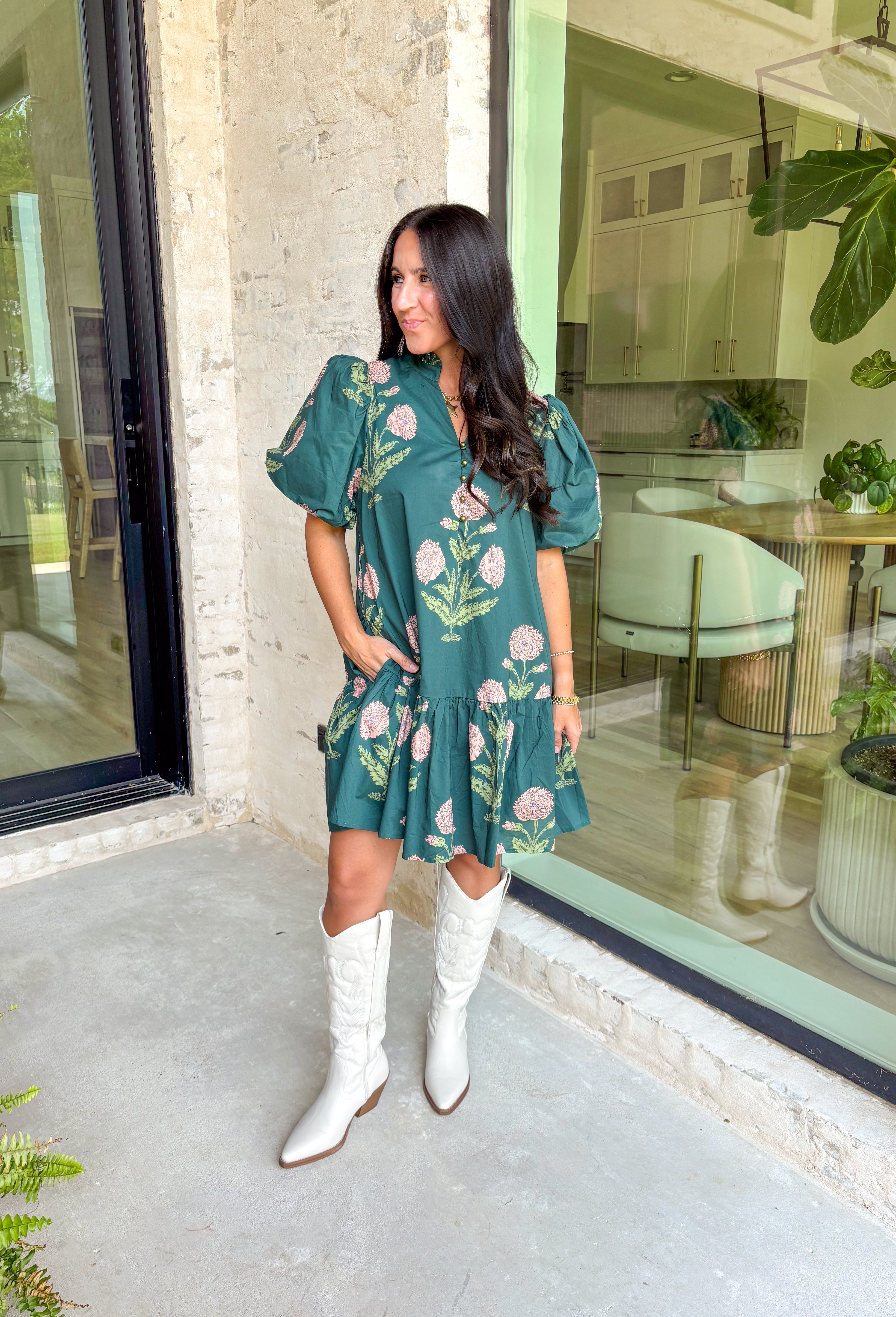 Rich, romantic, and made for fall days, this hunter green mini dress is covered in a warm seasonal floral print. The ruffle neck band collar with gold accent button closure adds a polished touch, while the short bubble sleeves and flouncy ruffle hem keep it playful and feminine. Side pockets bring in that practical detail we love, and the fully lined cotton design makes it comfortable from day to night. Perfect for everything from brunch to seasonal gatherings.