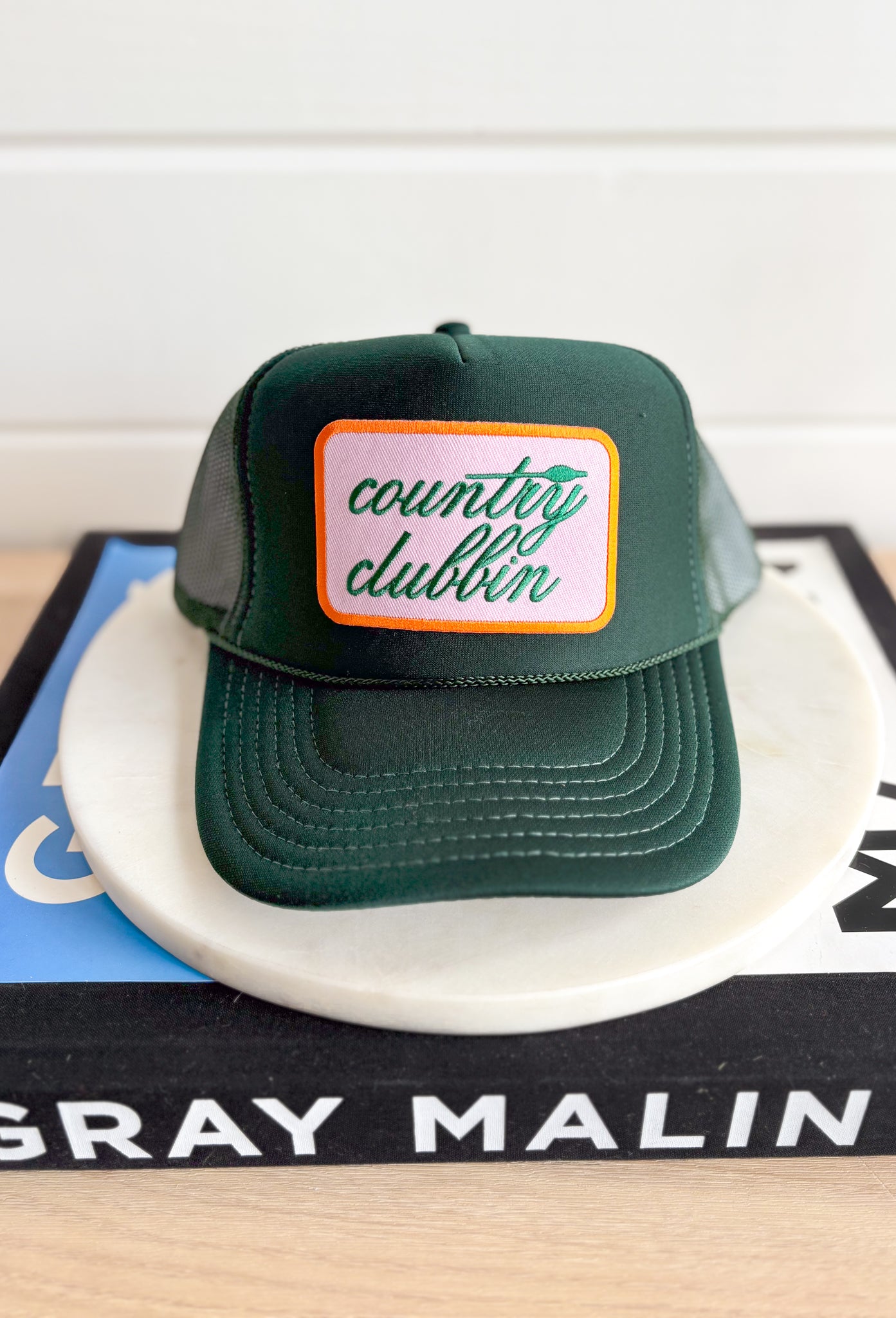 Country Clubbin' Trucker Hat, forest green trucker hat with orange and pink patch in the center of the hat with forest green embroidered text "country clubbin"