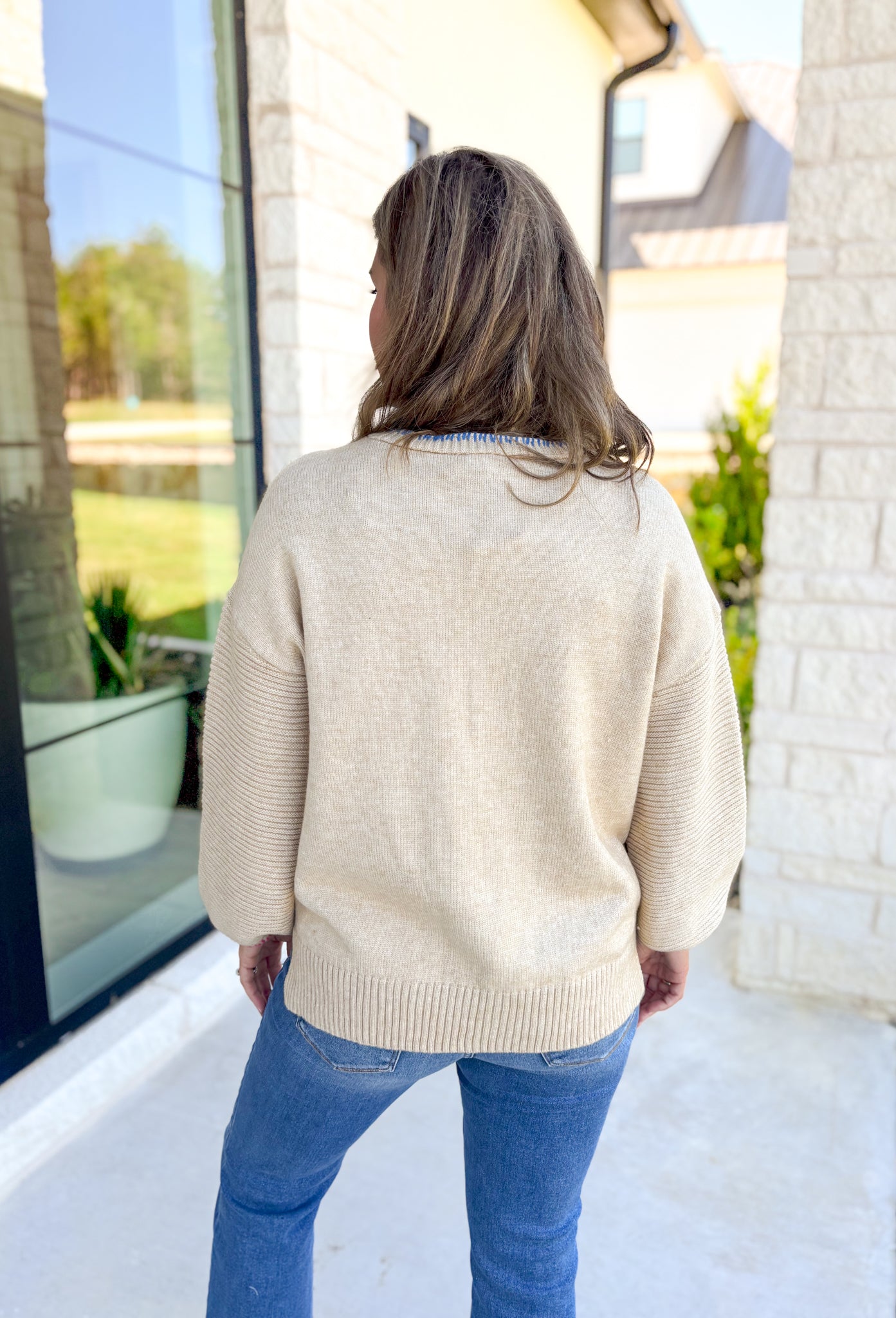 Cozy Cider Knit Sweater, tan knit sweater with ribbing on the sleeves, v-neck line, quarter button down detail, blue whipstitching on the neck line, orange whipstitching along the button down, hot pink whipstitching around the wrists 