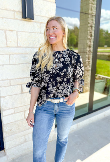 Full Of Surprises Blouse, black, taupe, and white floral quarter sleeve blouse with tie detail on the hem of the sleeves, grey and white piping on the hem of the bow and sleeves 