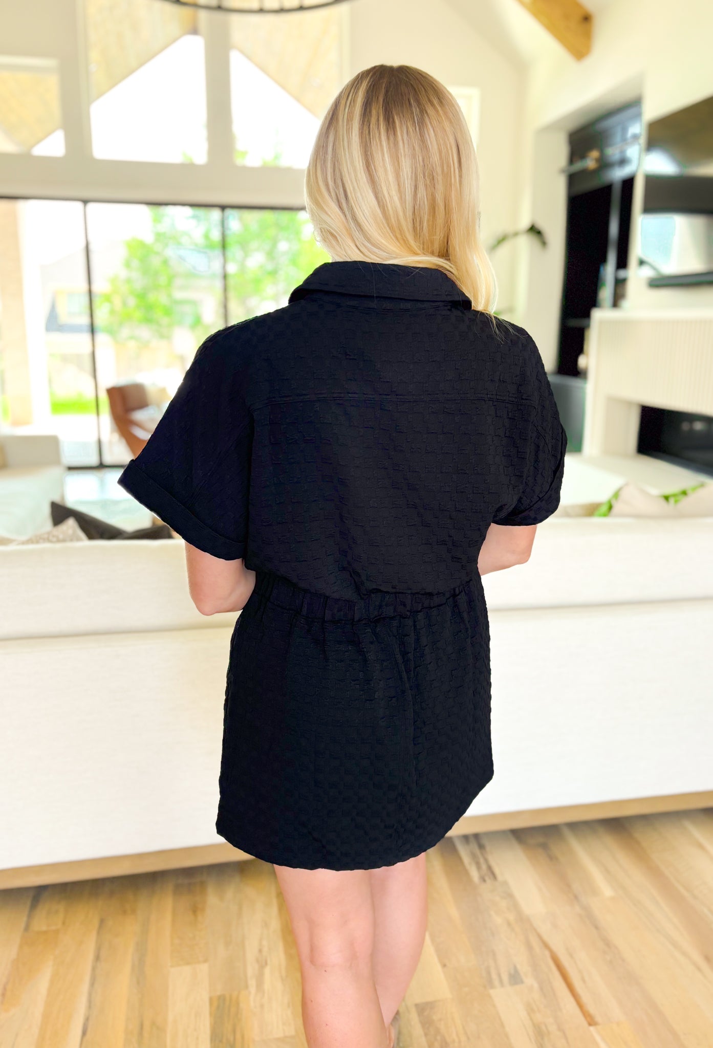 Hard To Leave Dress, black checkered textured dress with built in shorts underneath, button down detail with wooden buttons, cinching at the waist, pockets, and rolled sleeves