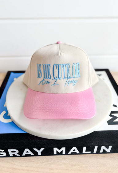 Is He Cute Trucker Hat, bone and light pink trucker hat with light blue embroidered text "is he cute or am I tipsy"