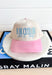 Is He Cute Trucker Hat, bone and light pink trucker hat with light blue embroidered text "is he cute or am I tipsy"