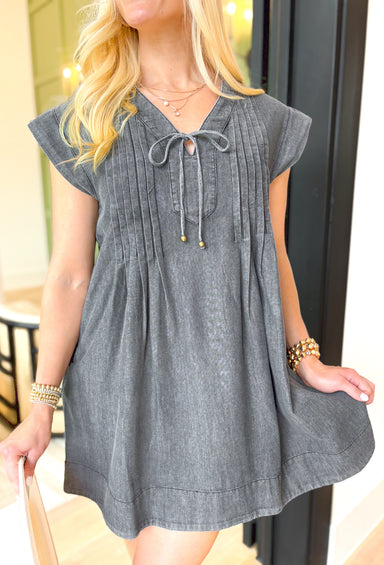 Lucky Me Denim Dress, washed charcoal denim dress with cap sleeves, v-neckline, pleating across the chest, pockets, and bow detail on  the bottom of the neckline