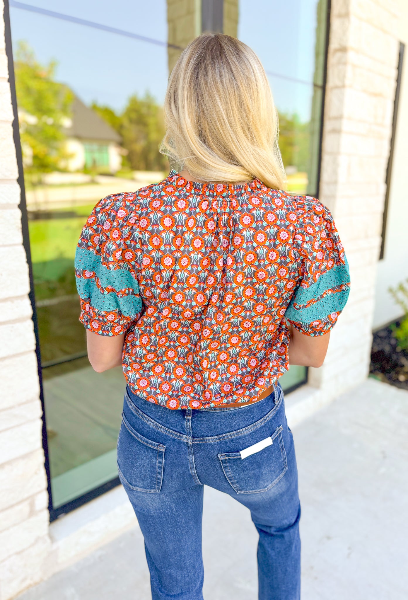 Nothing Has Changed Top, short puff sleeve blouse with v-neck line that has ruffles lining it, abstract print in the colors orange, periwinkle, cream, grey, and turquoise. Turquoise lace details on the puff sleeves 