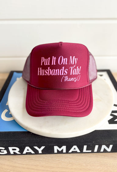 Husbands Tab Trucker Hat, maroon trucker hat with bubble gum pink text on the front "put it on my husbands tab! (thanks!)"