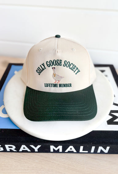 Silly Goose Society Trucker Hat, dark green and cream trucker hat with dark green embroidered text "silly goose society, lifetime member" and an embroidered good in the middle with sunglasses and a chain on 