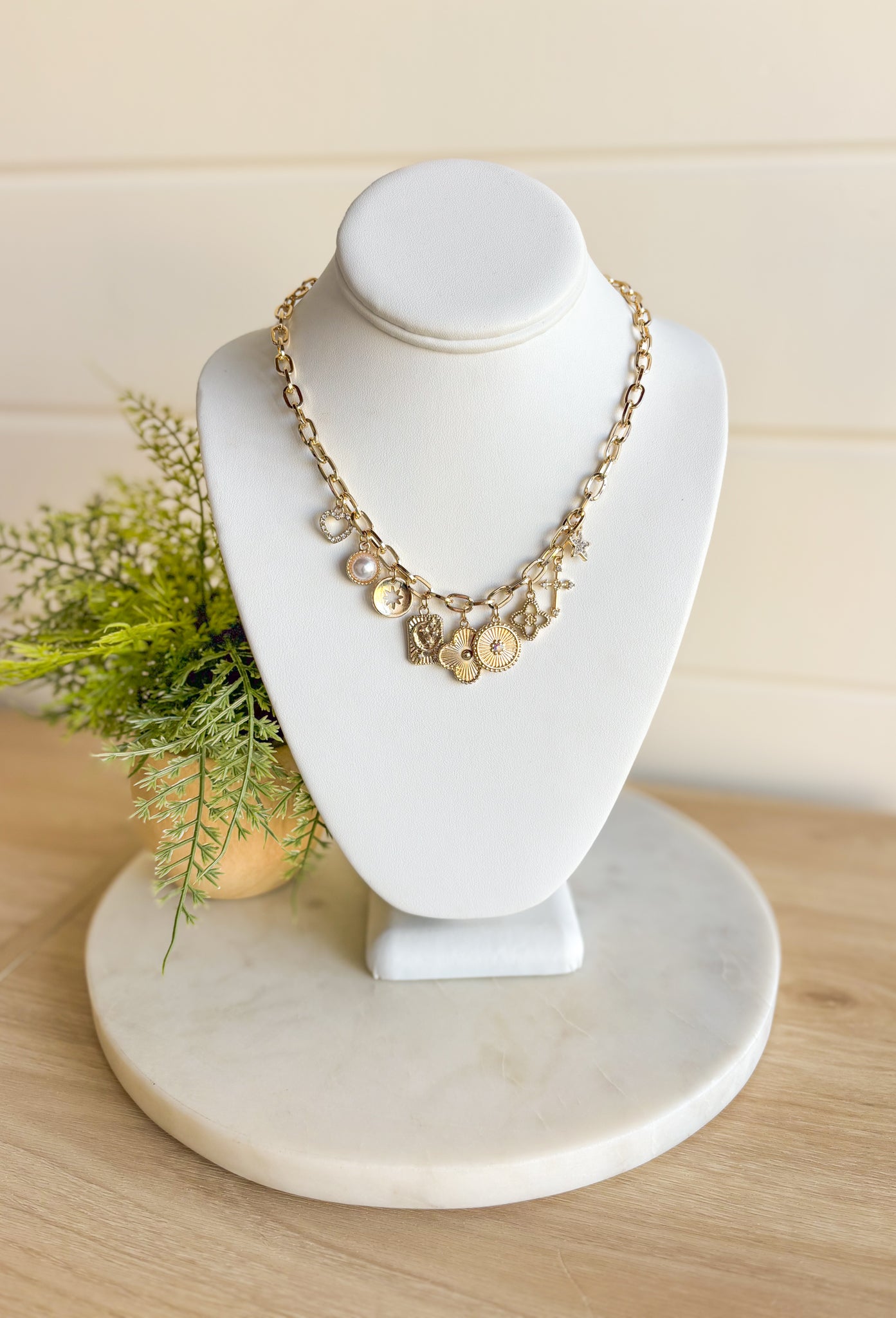 Talk About It Necklace, gold paper chain link necklace with a variation of gold charms with different details on them such as pearls, diamonds, and other designs 