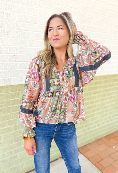 Walking In The Wind Top, long blouse sleeve top with ruffling on the neck like and wrists. abstract floral pattern in the colors terracotta, blue-grey, sage green, fuchsia, cream, red, and charcoal grey. Charcoal grey lace detail on the chest and sleeves