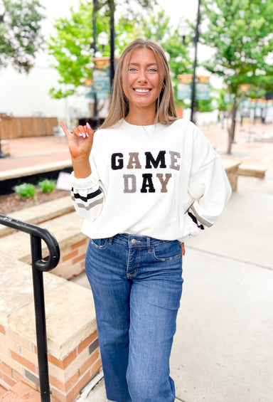 Z SUPPLY Oversized Game Day Sweatshirt in Bone, white crewneck with "game day" spelt out in black, gray, and taupe patches, sleeves have a taupe and black stripe on the wrist 