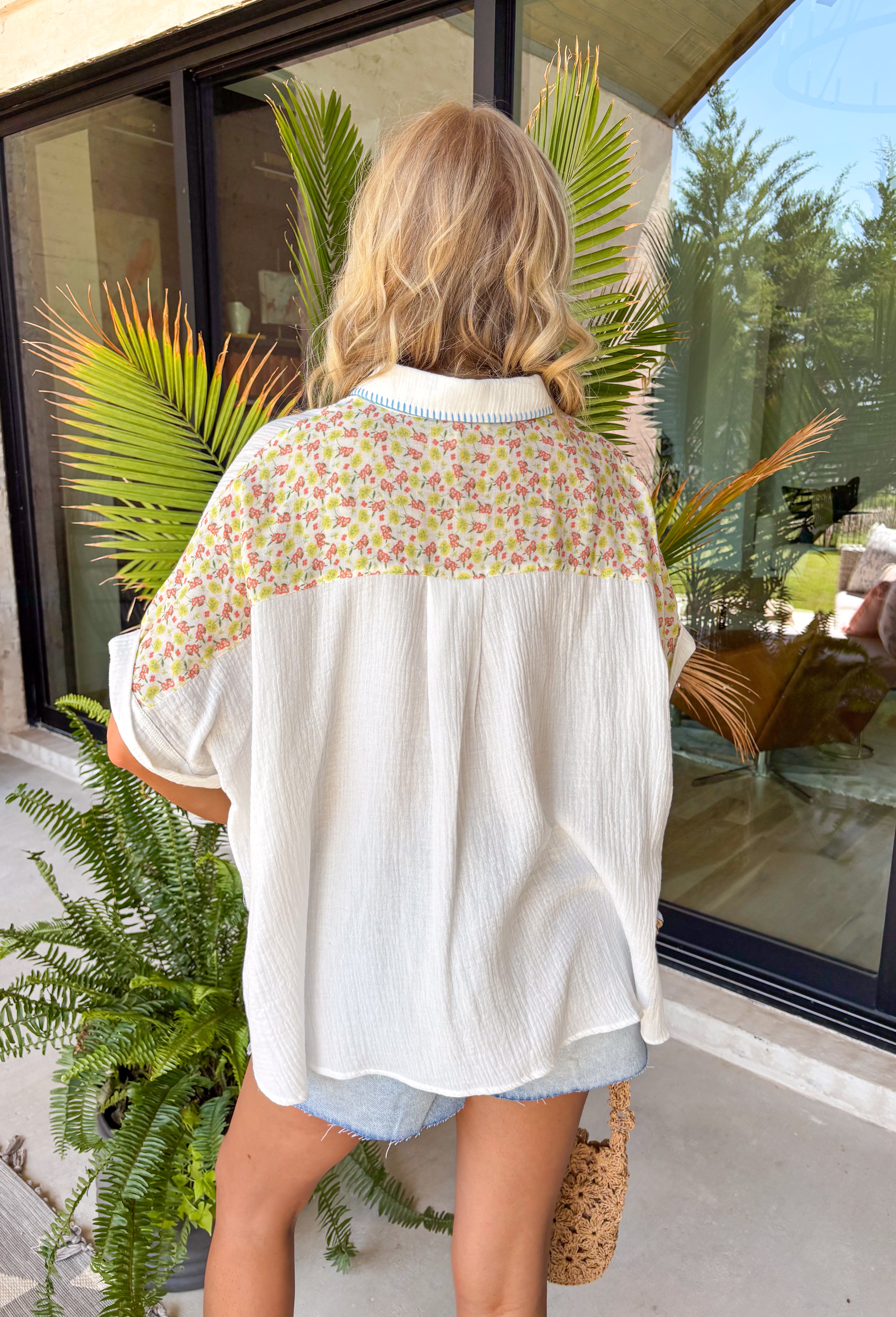 This white gauze button down top is bringing all the fun, feel-good summer vibes! With its colorful floral print in shades of blue, green, pink, yellow, and orange, plus the cutest purple and white gingham details, it has that playful patchwork-inspired look that totally stands out. The lightweight gauze fabric keeps it breathable and easy for hot days, while the collared neckline adds a touch of structure. It’s one of those tops that instantly brightens your outfit—just pair it with denim or shorts and go.