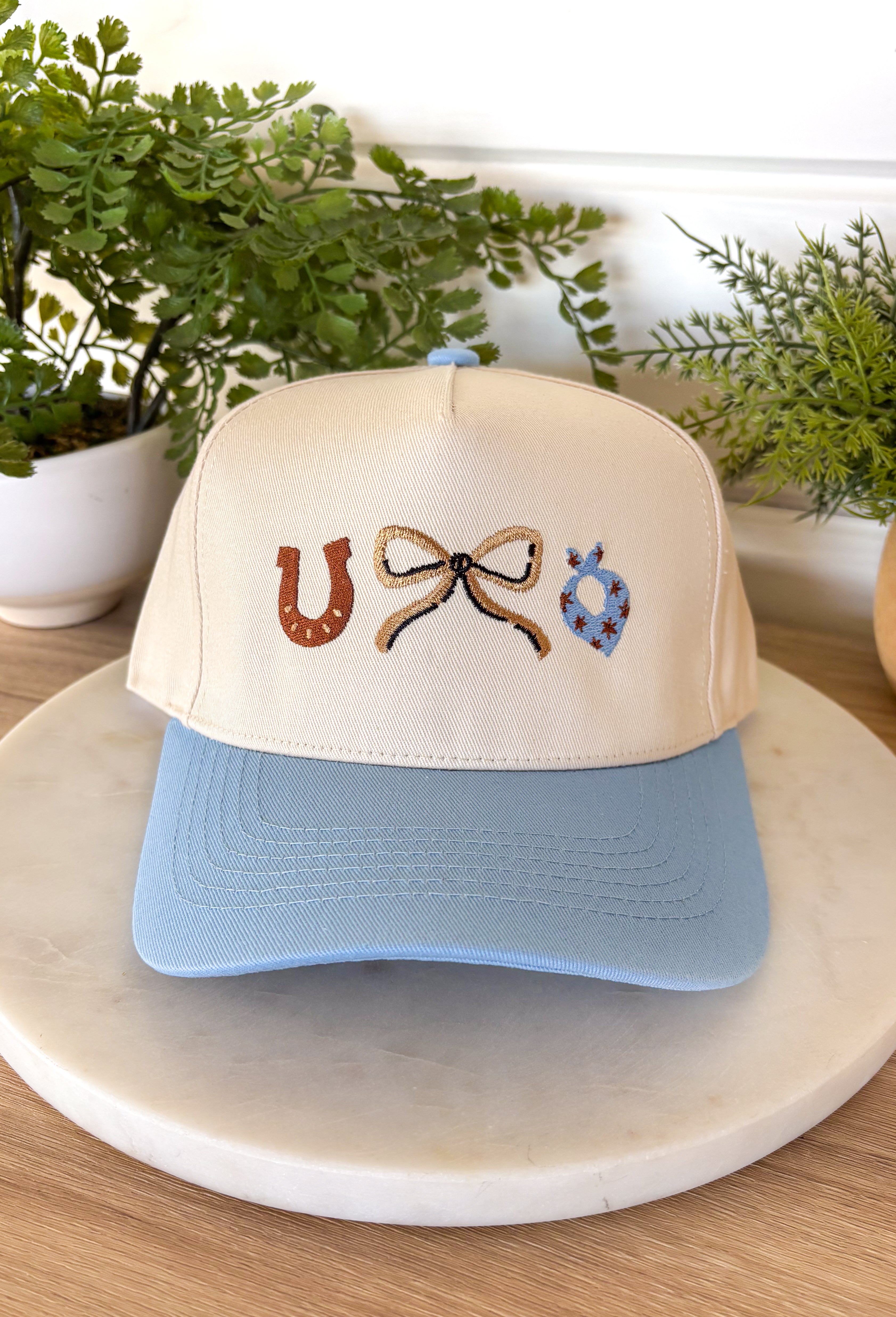 This neutral trucker hat is finished with a soft light blue bill for a fresh, easygoing look. Featuring an embroidered western-inspired design on the front, it adds just the right amount of character while staying effortlessly wearable. The adjustable back ensures a comfortable fit, making it perfect for everyday errands, outdoor plans, or topping off a casual outfit.