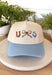 This neutral trucker hat is finished with a soft light blue bill for a fresh, easygoing look. Featuring an embroidered western-inspired design on the front, it adds just the right amount of character while staying effortlessly wearable. The adjustable back ensures a comfortable fit, making it perfect for everyday errands, outdoor plans, or topping off a casual outfit.