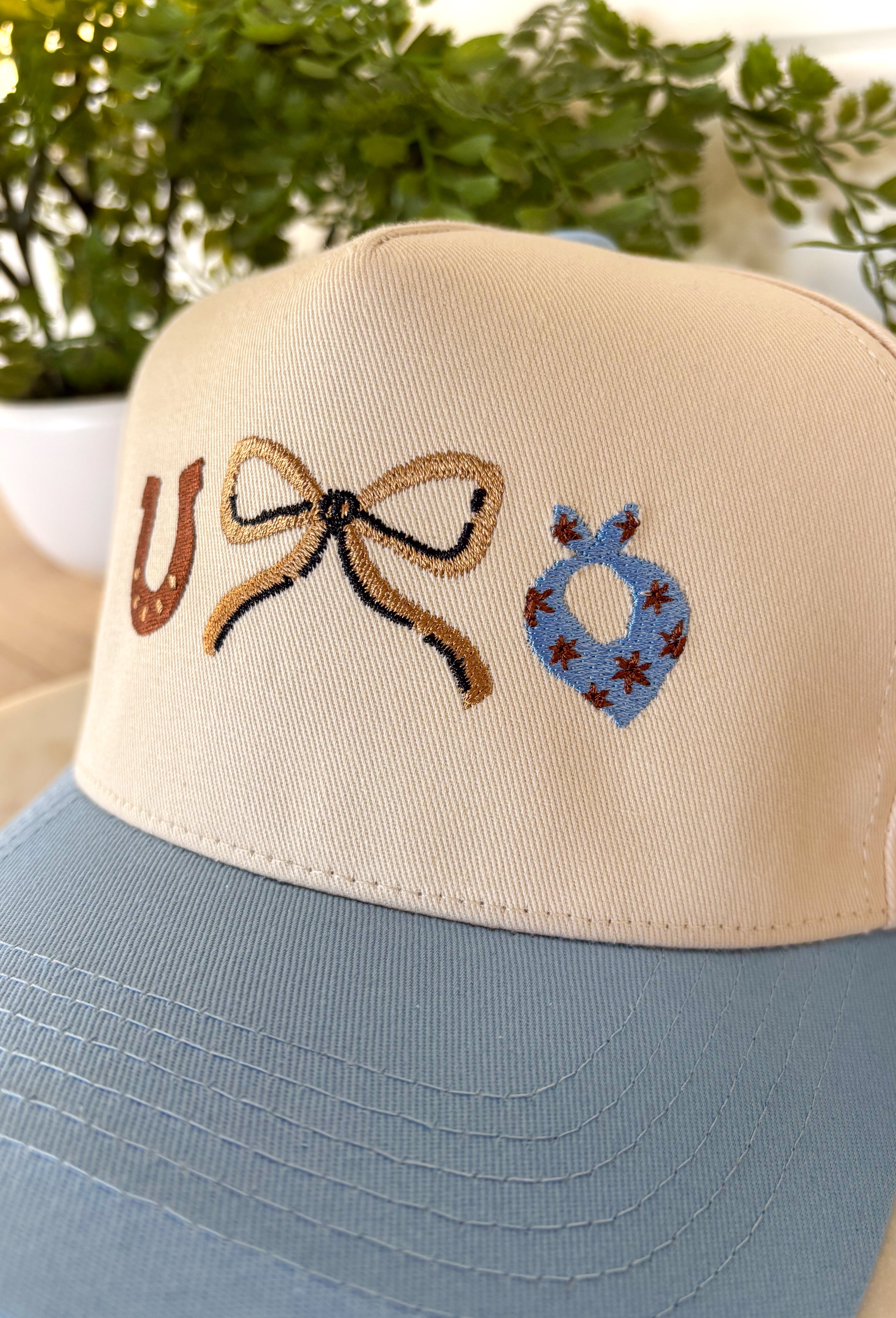 This neutral trucker hat is finished with a soft light blue bill for a fresh, easygoing look. Featuring an embroidered western-inspired design on the front, it adds just the right amount of character while staying effortlessly wearable. The adjustable back ensures a comfortable fit, making it perfect for everyday errands, outdoor plans, or topping off a casual outfit.